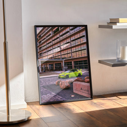 Framed Mitsubishi Evo 9 poster with vibrant green car and modern urban background wall art leaned against a white wall.