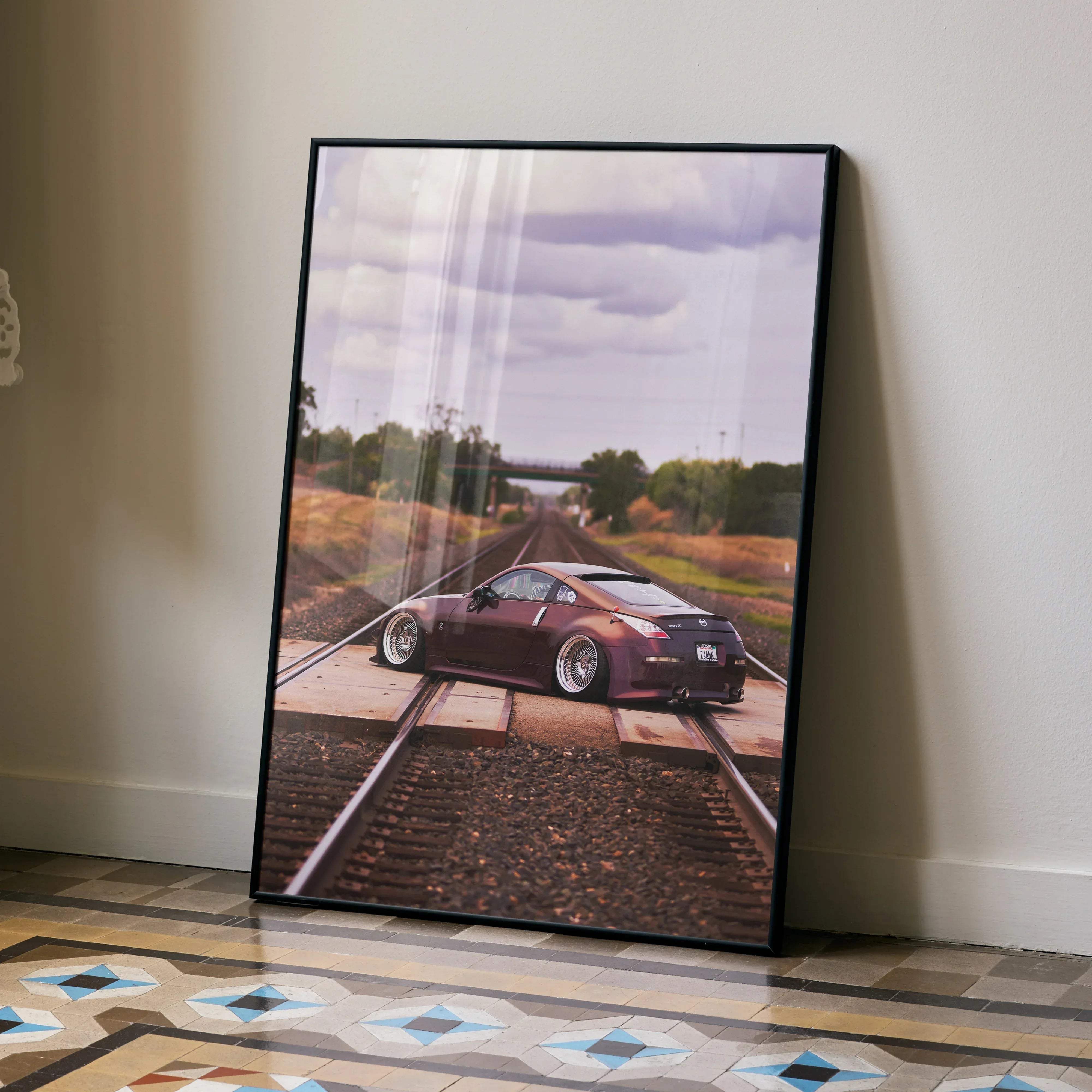 A framed maroon Nissan 350Z sports car poster on railway tracks in a sleek black frame for car lovers wall decor