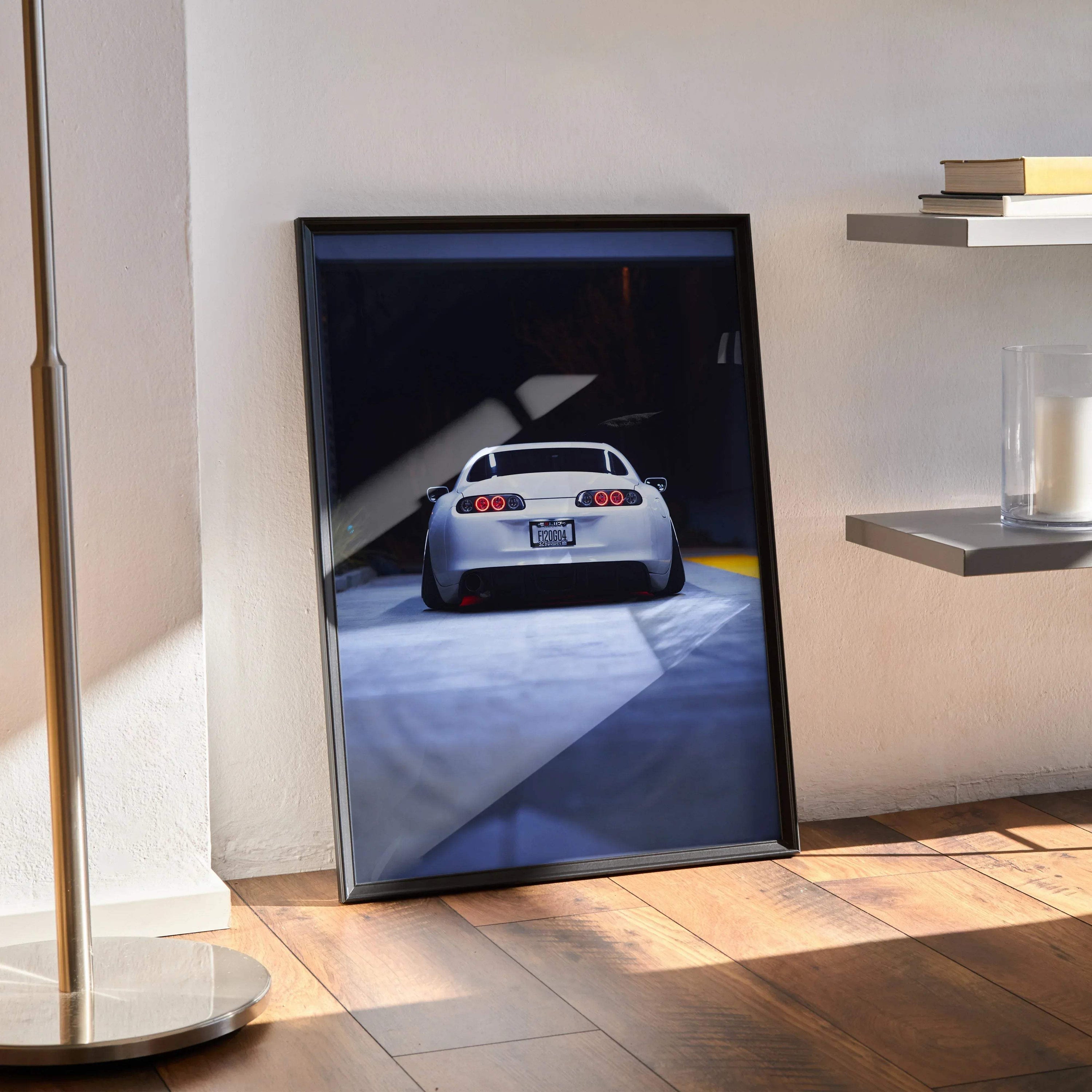 Toyota Supra MK4 rear view poster with dark background, framed wall art leaning on floor.