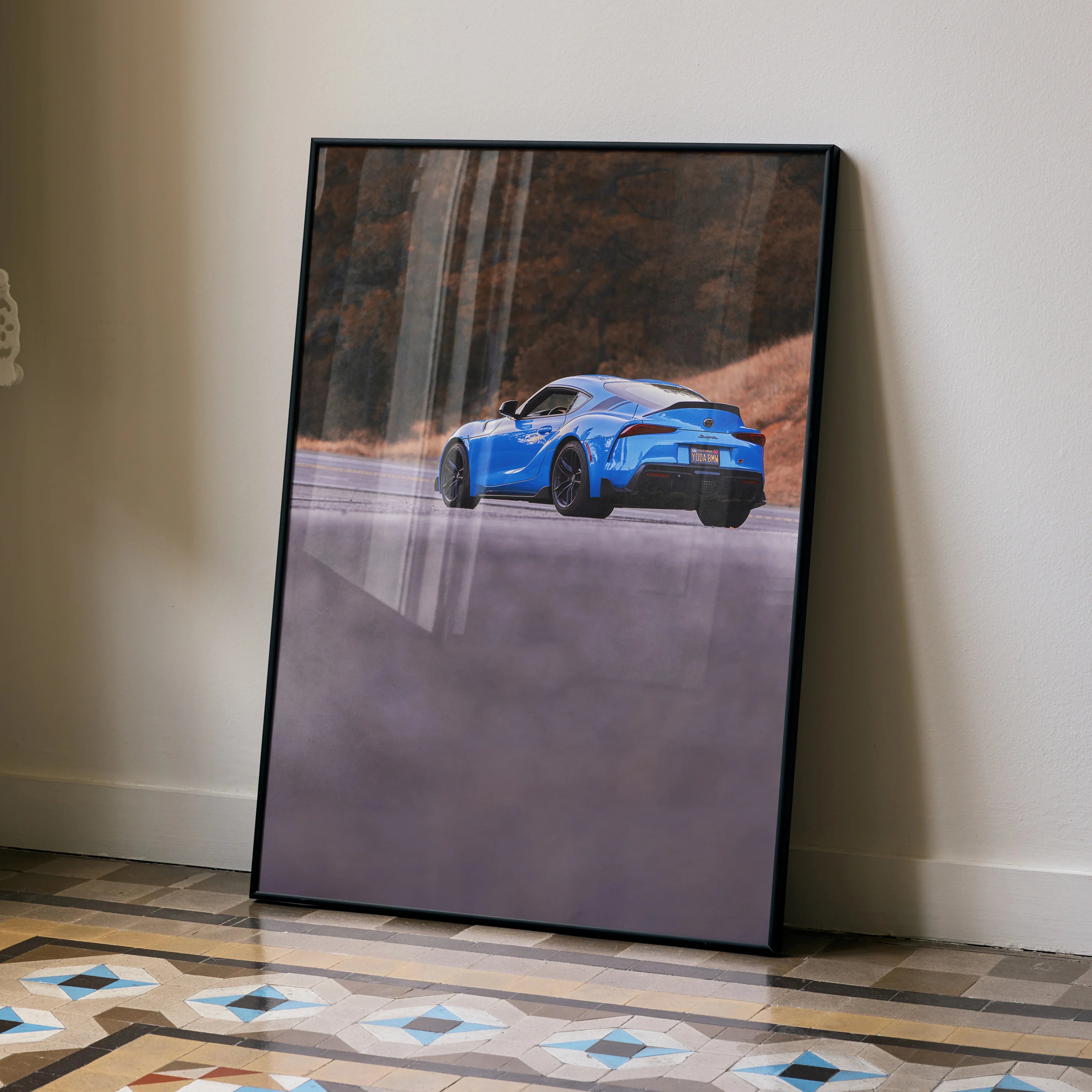 Toyota Supra MK5 in blue on a scenic road poster with black frame, automotive wall art.
