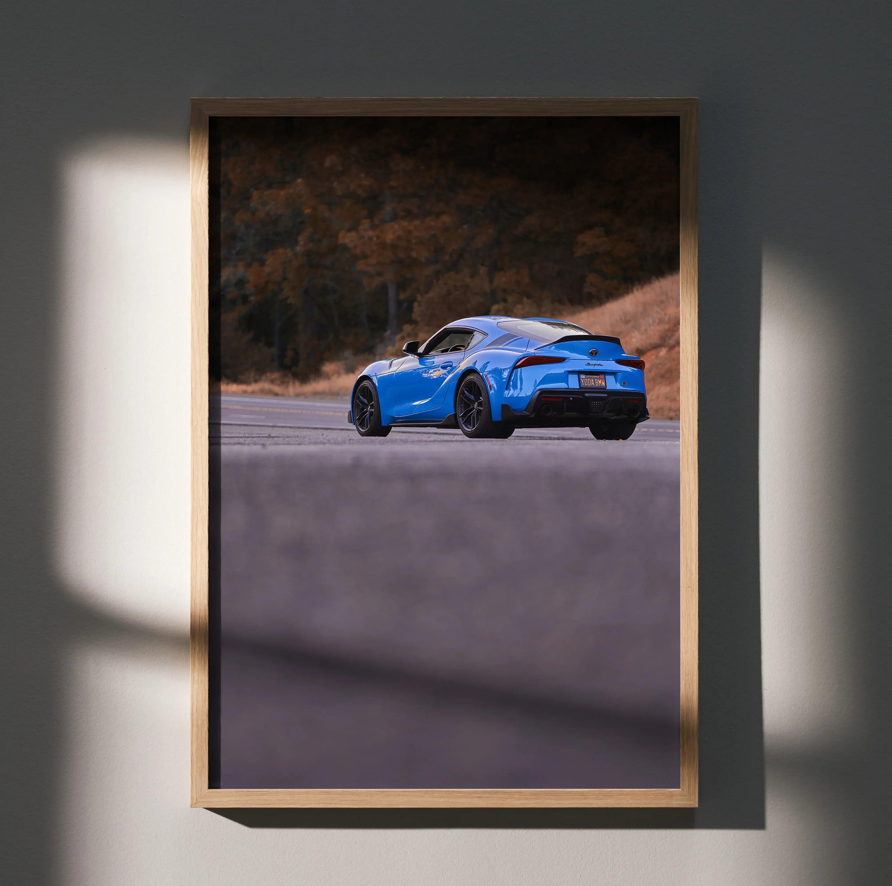 Toyota Supra MK5 in blue driving on winding road poster wall art with autumn trees backdrop.
