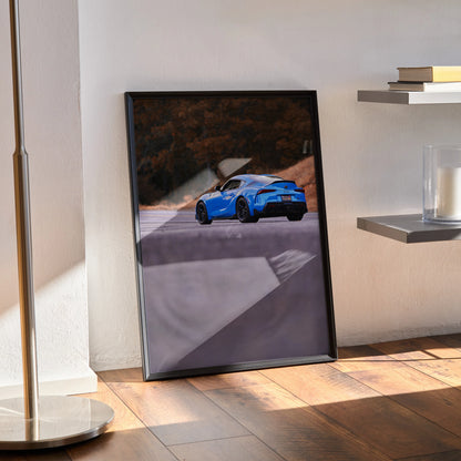 Toyota Supra MK5 driving on a curved road in a high-resolution poster, automotive wall art with dark frame.