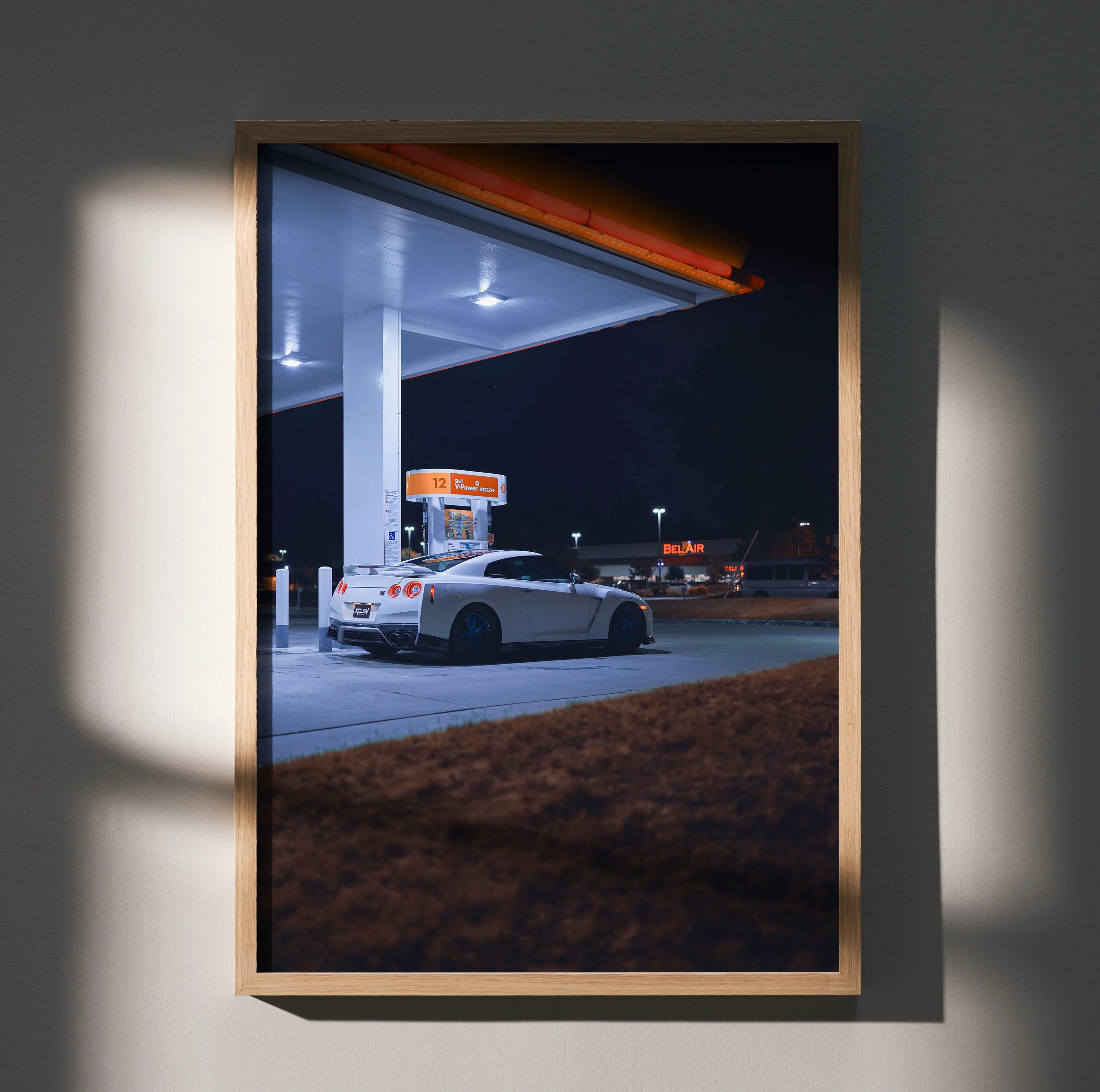 Framed poster wall art featuring a white Nissan GTR R35 parked at a night gas station under bright lights.