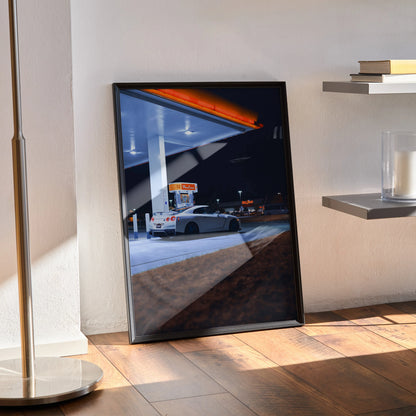 Nissan GTR R35 poster leaning against wall with nighttime gas station scene, sleek automotive wall art.