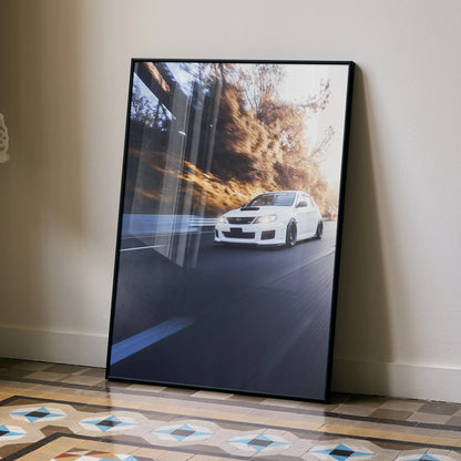 Subaru WRX STI racing on forest road poster wall art in black frame, leaning against beige wall.