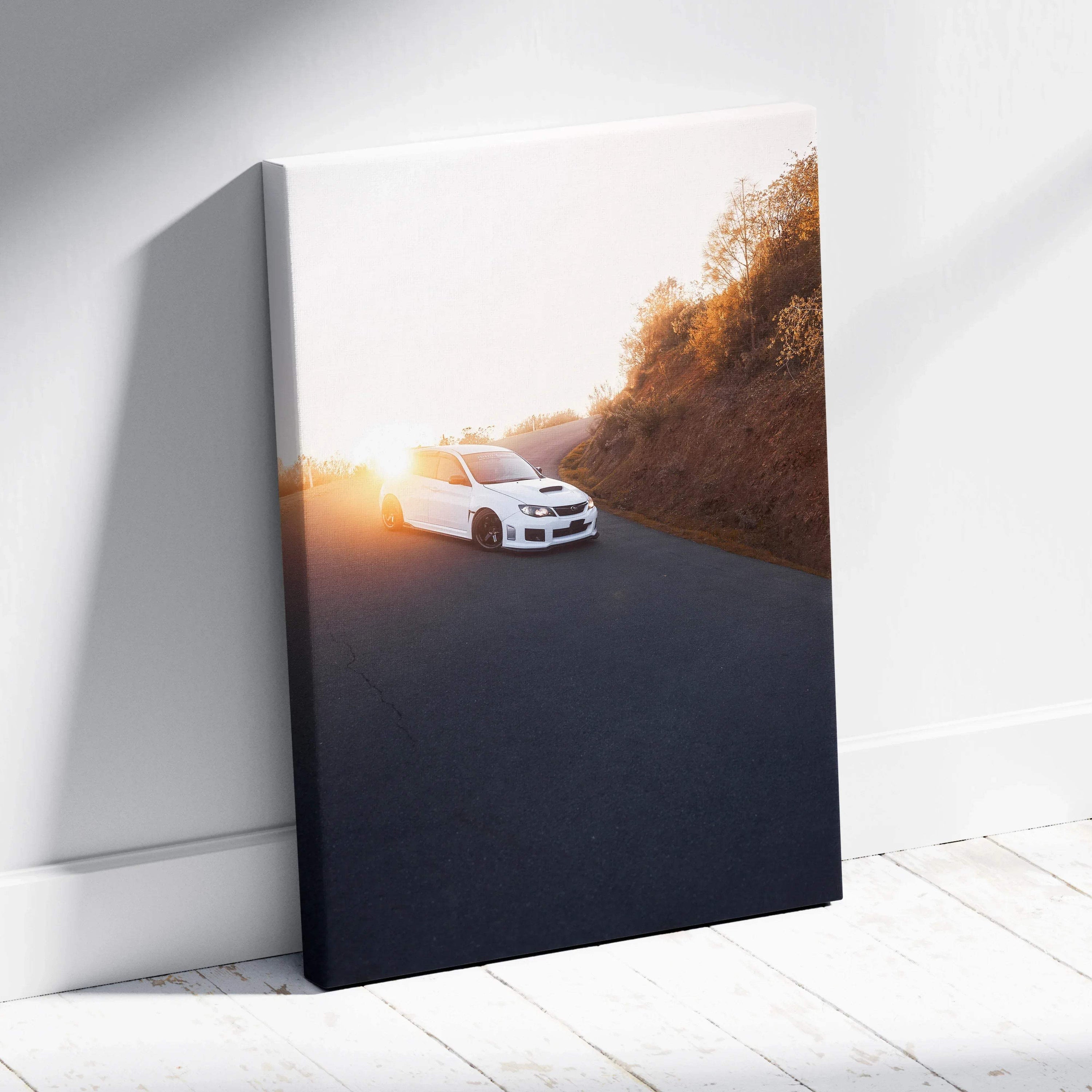 Vertical canvas wall art featuring a white Subaru WRX STI driving at sunset along a winding road.