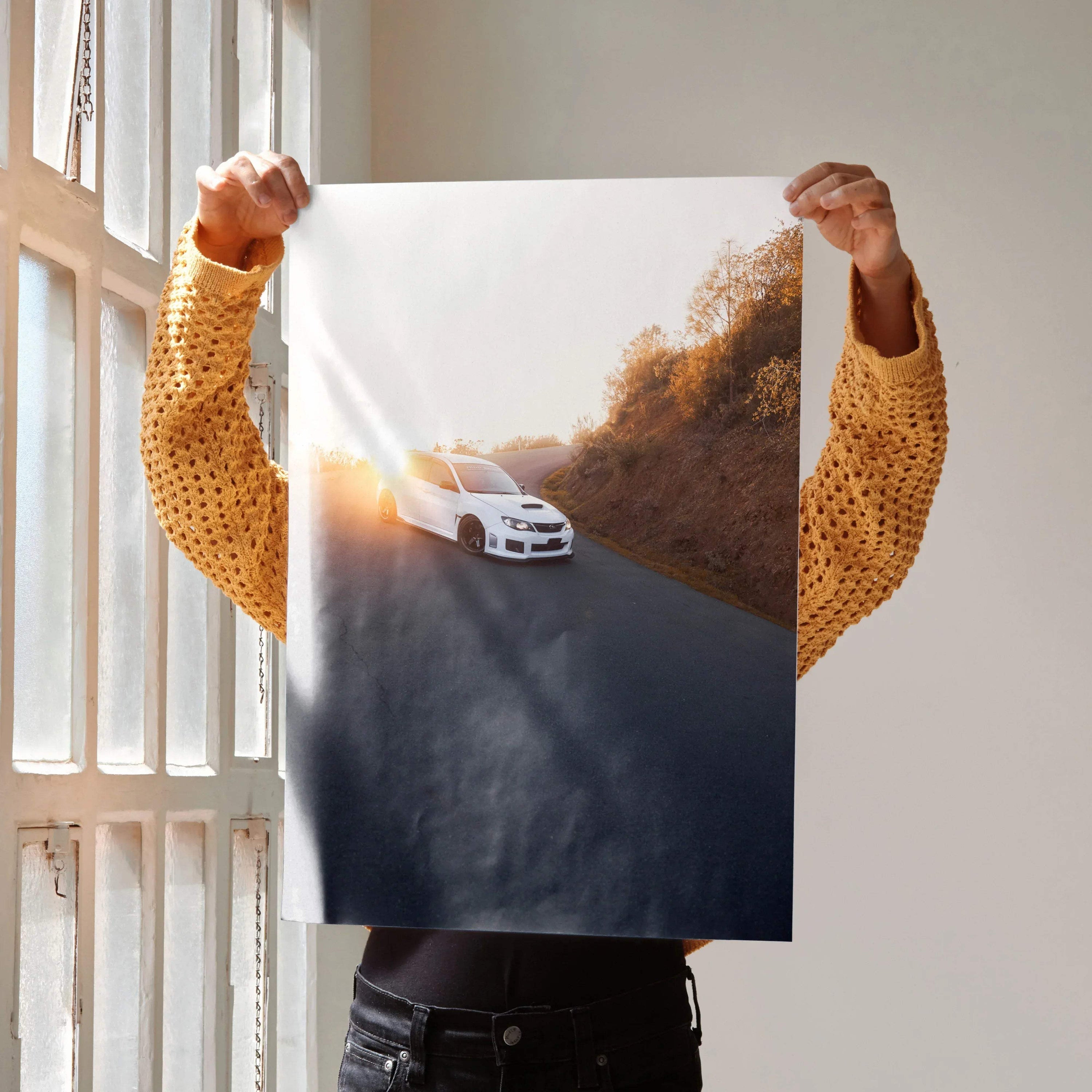 Subaru WRX STI poster wall art showing a white car driving on a hillside road at sunset.