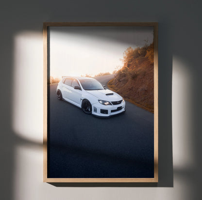 Subaru WRX STI poster wall art with white car driving on winding road at sunset.