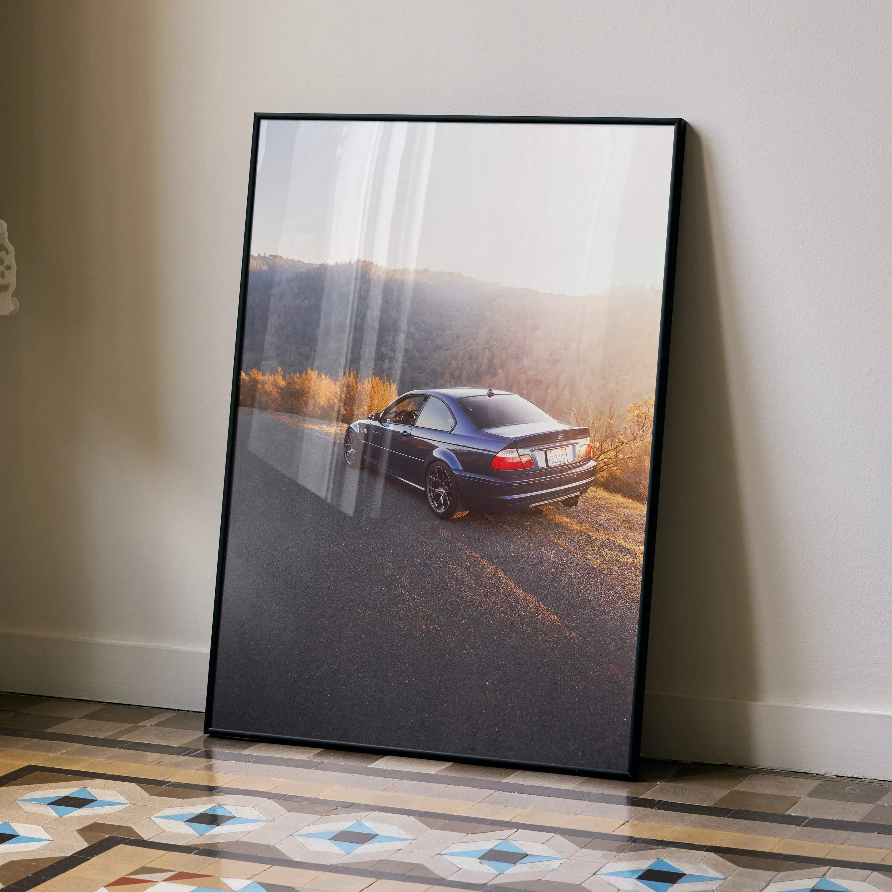 BMW E46 M3 driving on scenic road in sunset poster wall art with black frame.