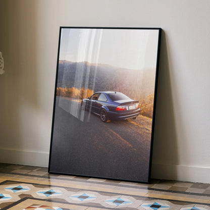 BMW E46 M3 driving on scenic road in sunset poster wall art with black frame.