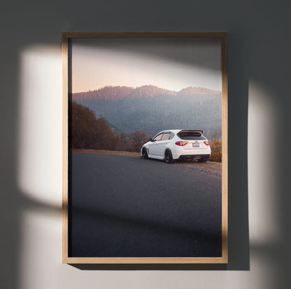 Subaru WRX STI driving on mountain road at sunset poster wall art in wooden frame.