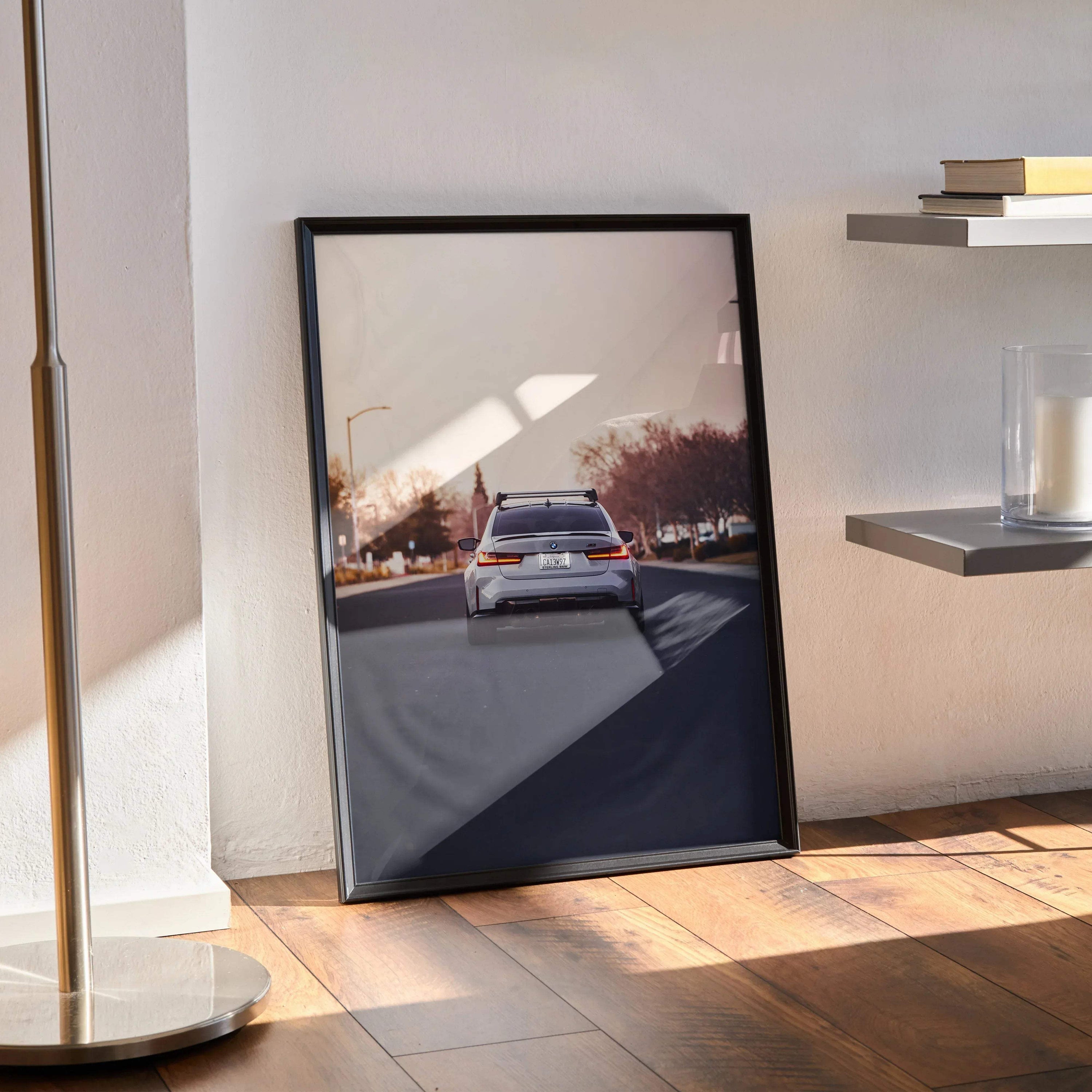 BMW G80 M3 high resolution poster leaning against wall, sleek black frame wall art with urban sunset background.