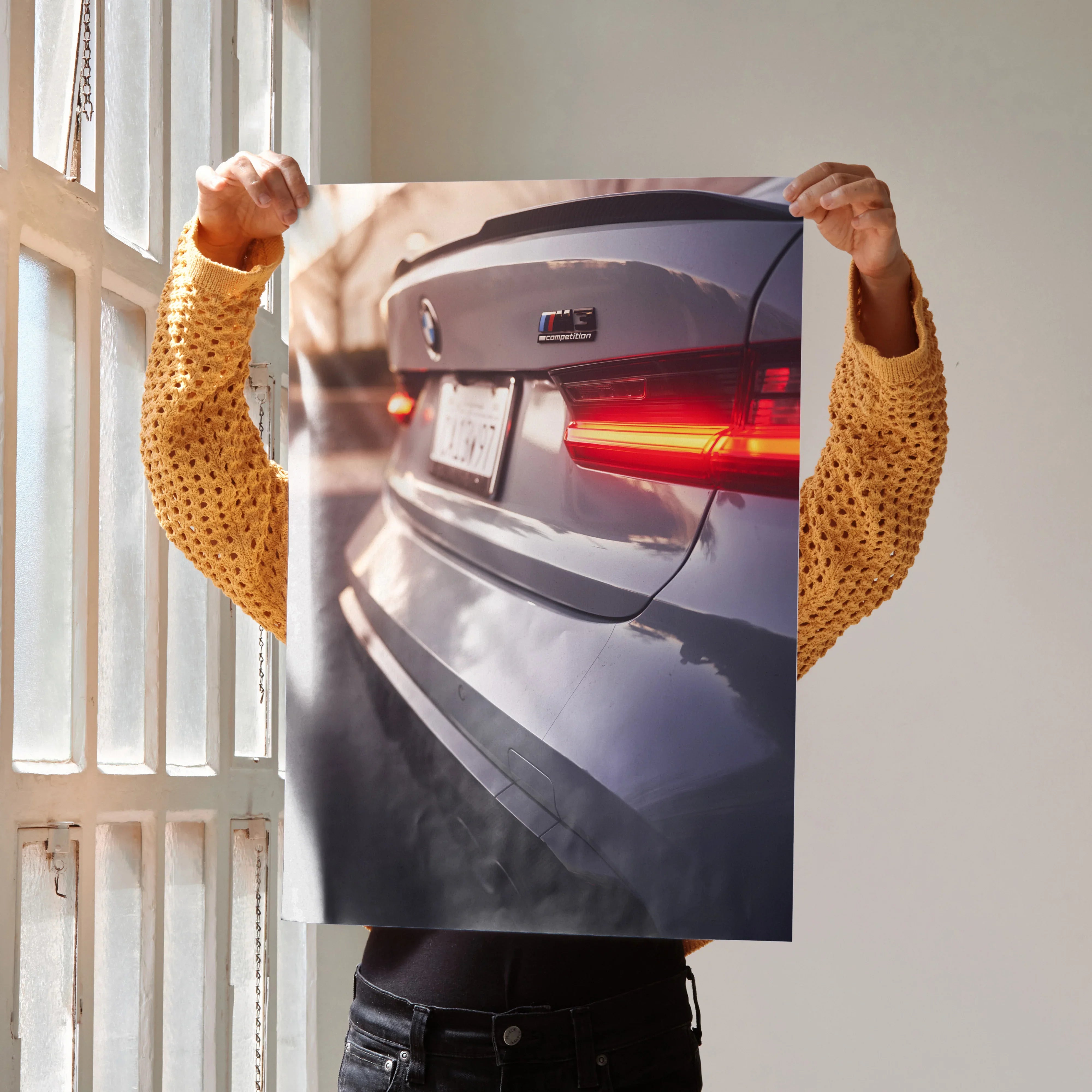 BMW G80 M3 rear close-up poster wall art held by person in yellow sweater near window light.