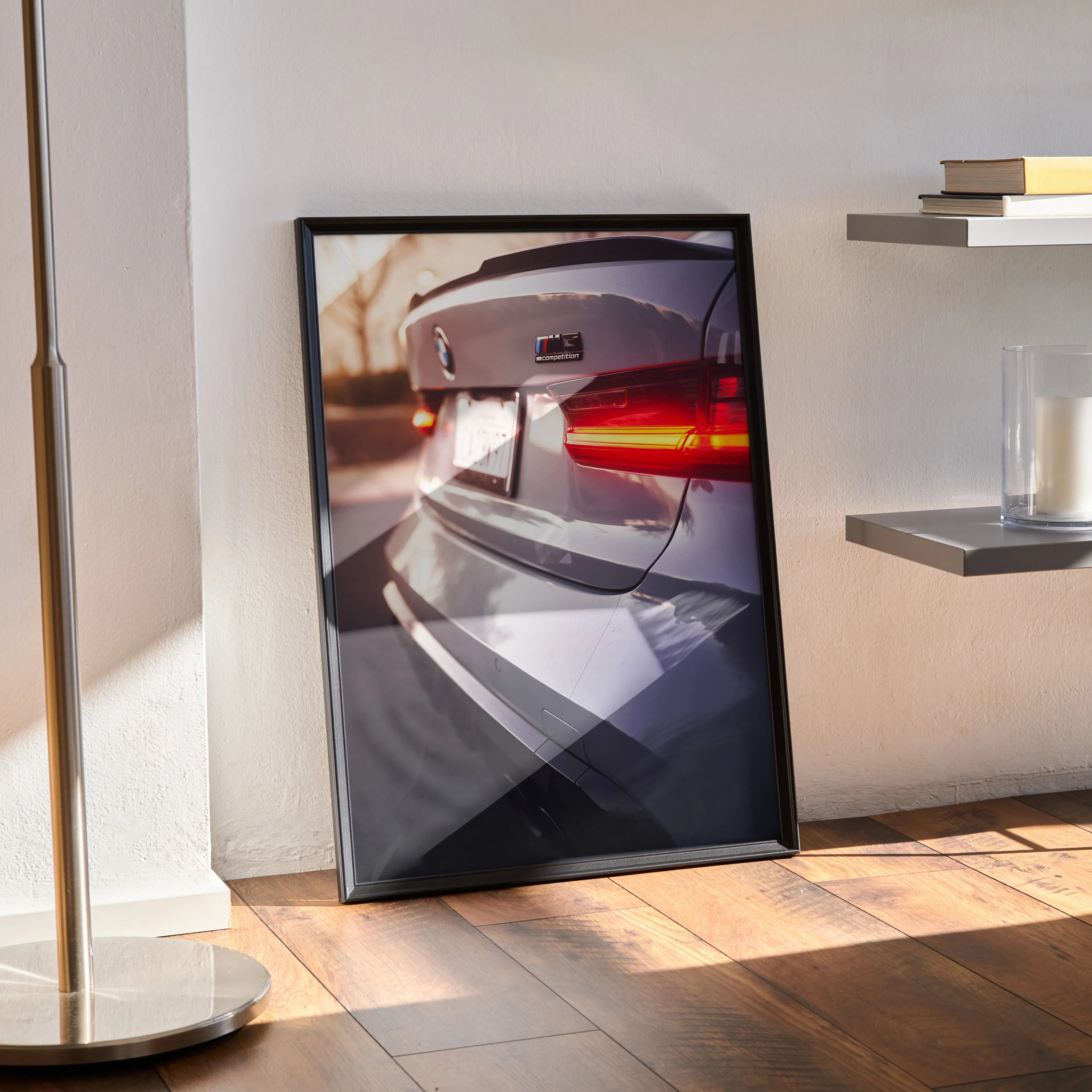 BMW G80 M3 rear view poster in black frame leaning on floor, automotive wall art with natural light shadows.