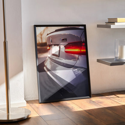 BMW G80 M3 rear view poster in black frame leaning on floor, automotive wall art with natural light shadows.