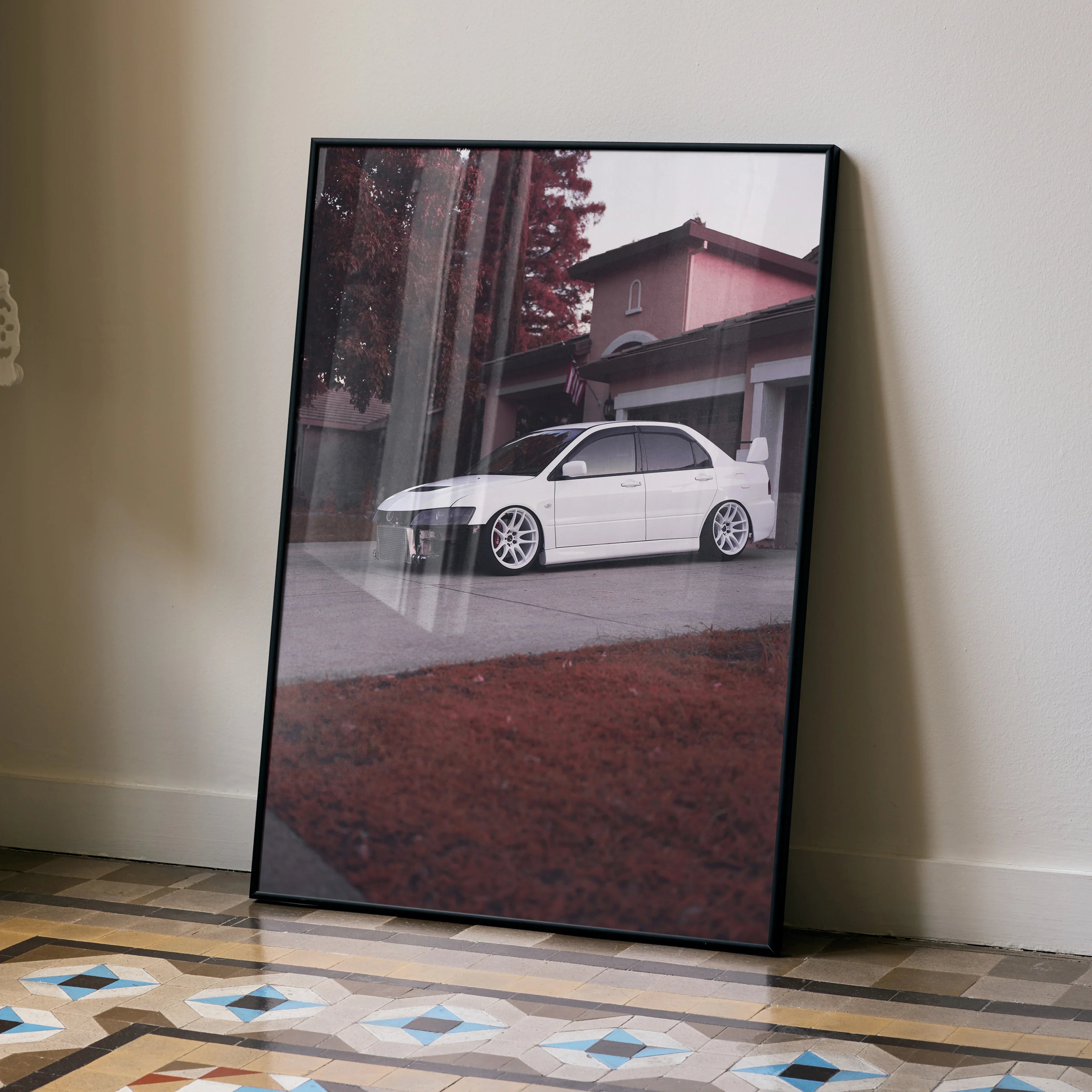 Mitsubishi Evo 8 poster in black frame leaning against beige wall, with autumn foliage background wall art.