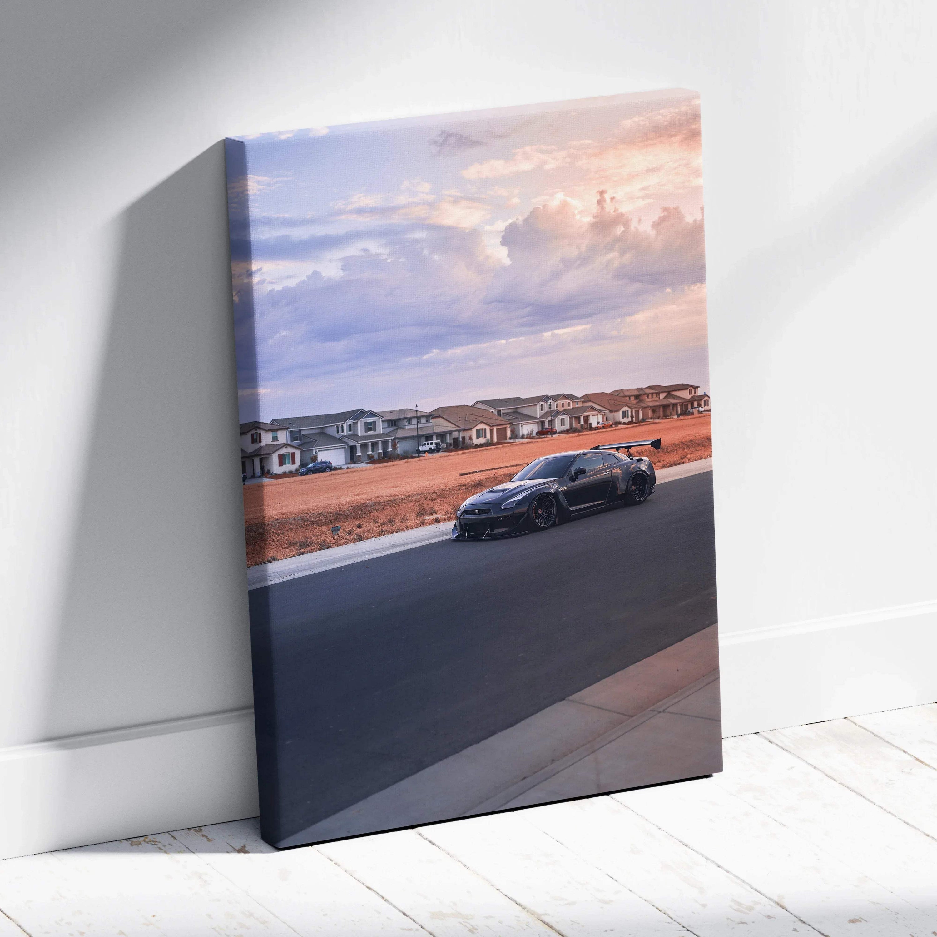 Vertical canvas wall art of a black Nissan R35 GTR parked on a road at sunset with houses in the background.