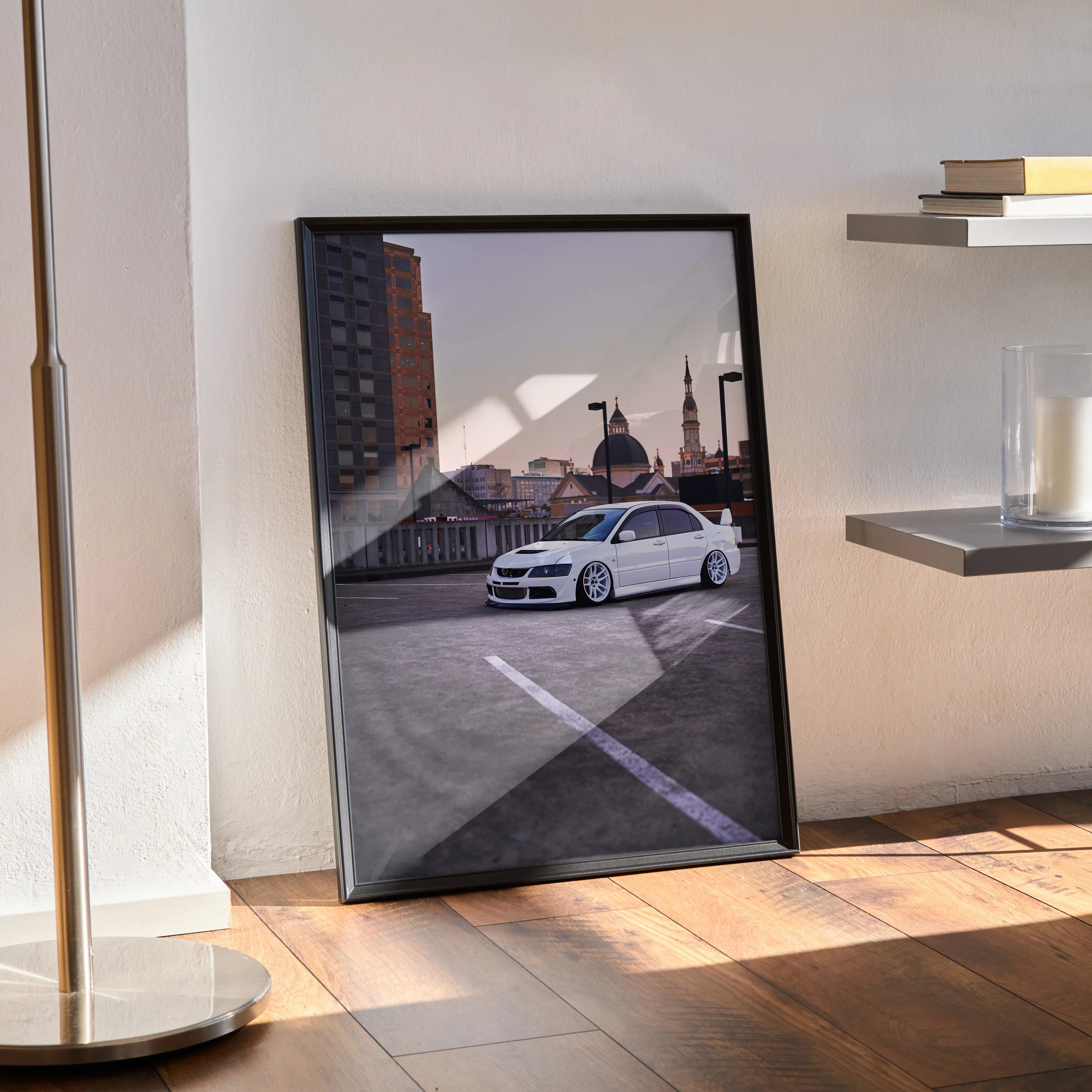 Mitsubishi Evo 8 poster wall art in black frame leaning against wall on wooden floor with modern shelving and lamp nearby.