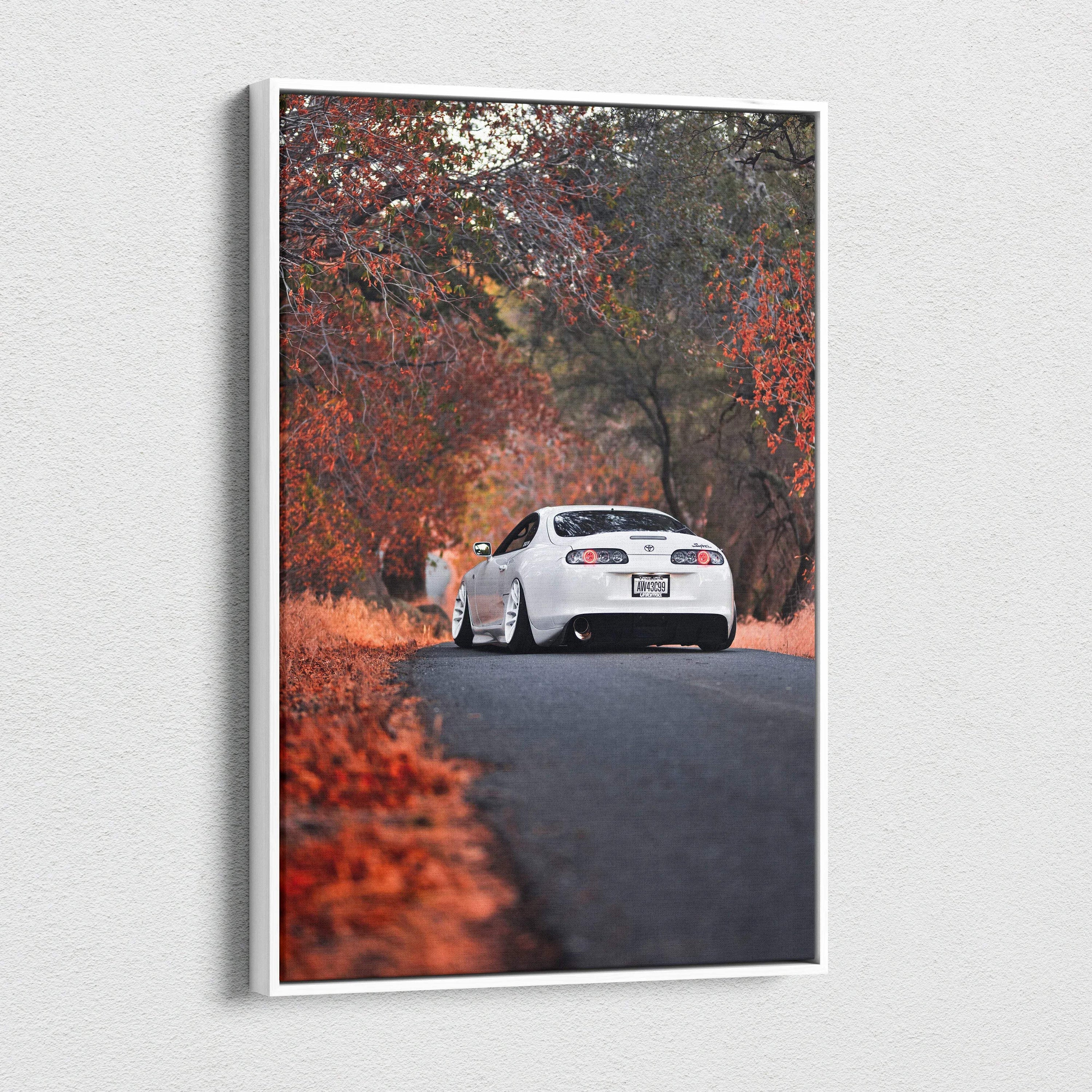 Vertical canvas wall art featuring a white Toyota Supra MK4 on a road surrounded by autumn trees and foliage.