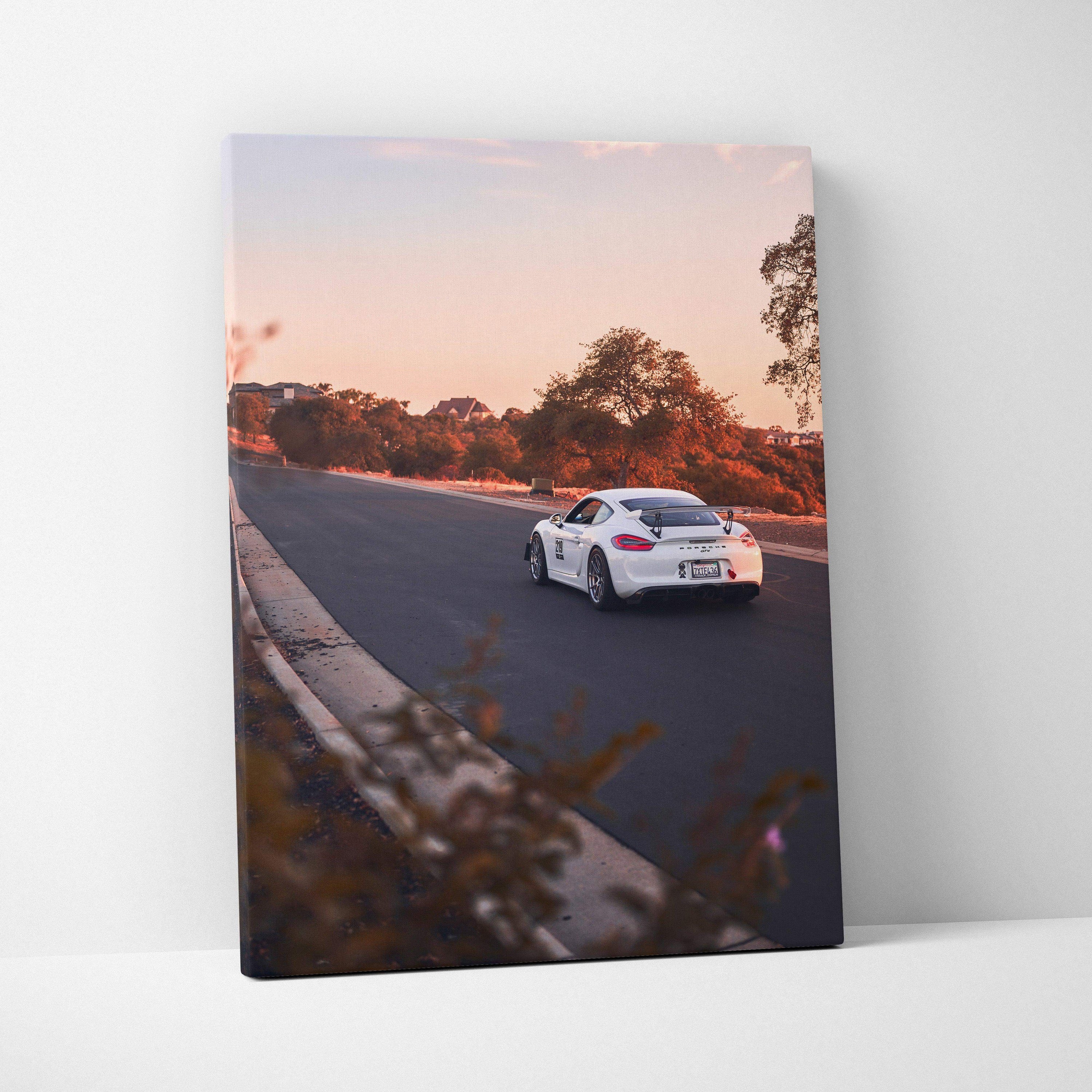 Vertical canvas wall art featuring a white Porsche GT4 racing on a sunset-lit track.