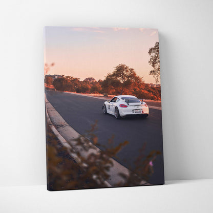 Vertical canvas wall art featuring a white Porsche GT4 racing on a sunset-lit track.