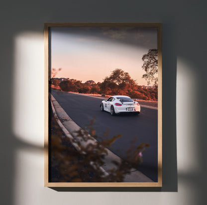 Porsche GT4 driving on road at sunset framed as premium wall art poster with warm tones.