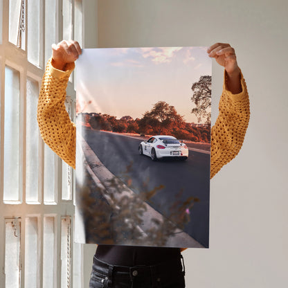 Porsche GT4 driving on a sunset road poster wall art with vibrant sky and trees.