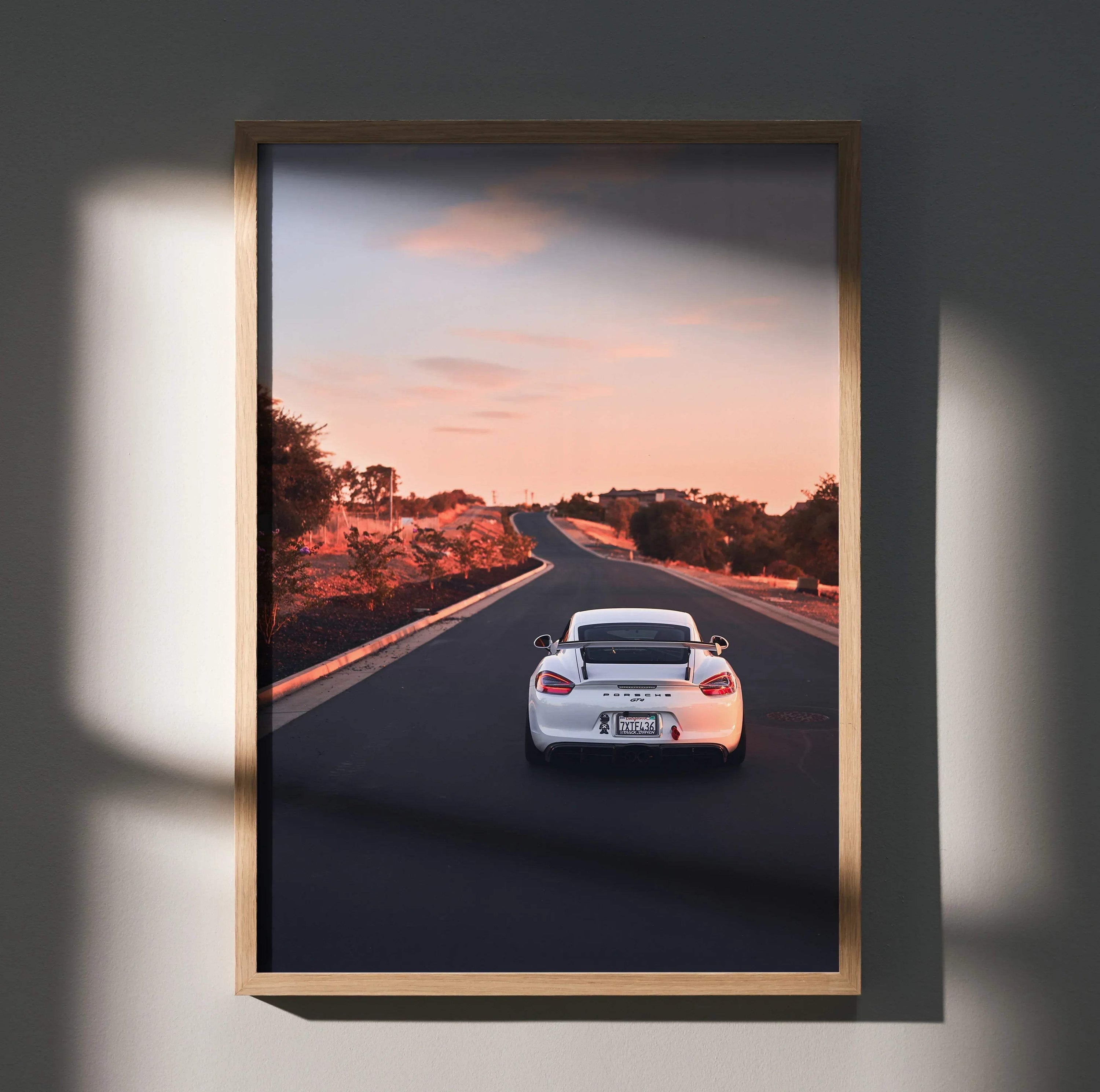 Porsche Cayman GT4 driving on open road at sunset poster wall art in wooden frame.