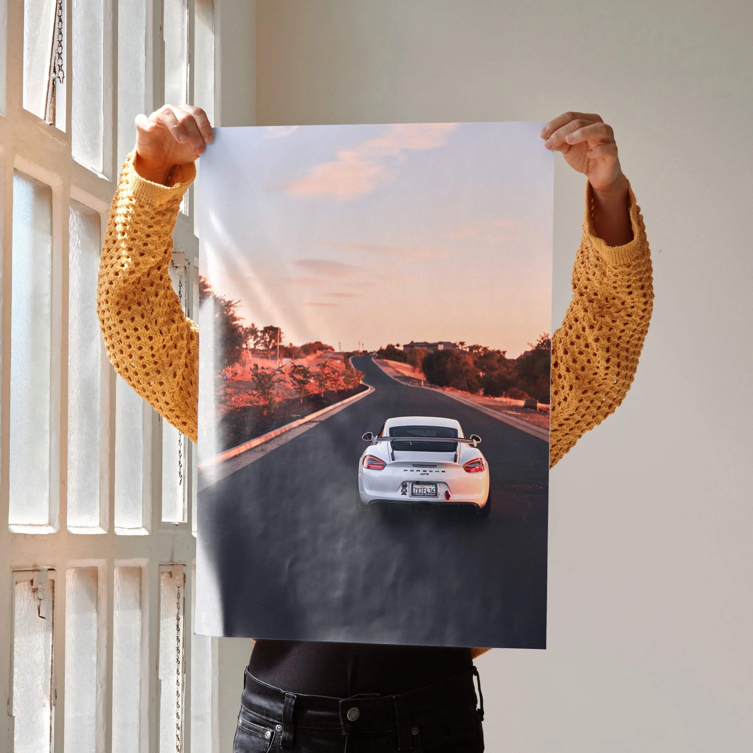 Porsche Cayman GT4 poster showing rear view on sunlit road, vibrant wall art with sunset sky.