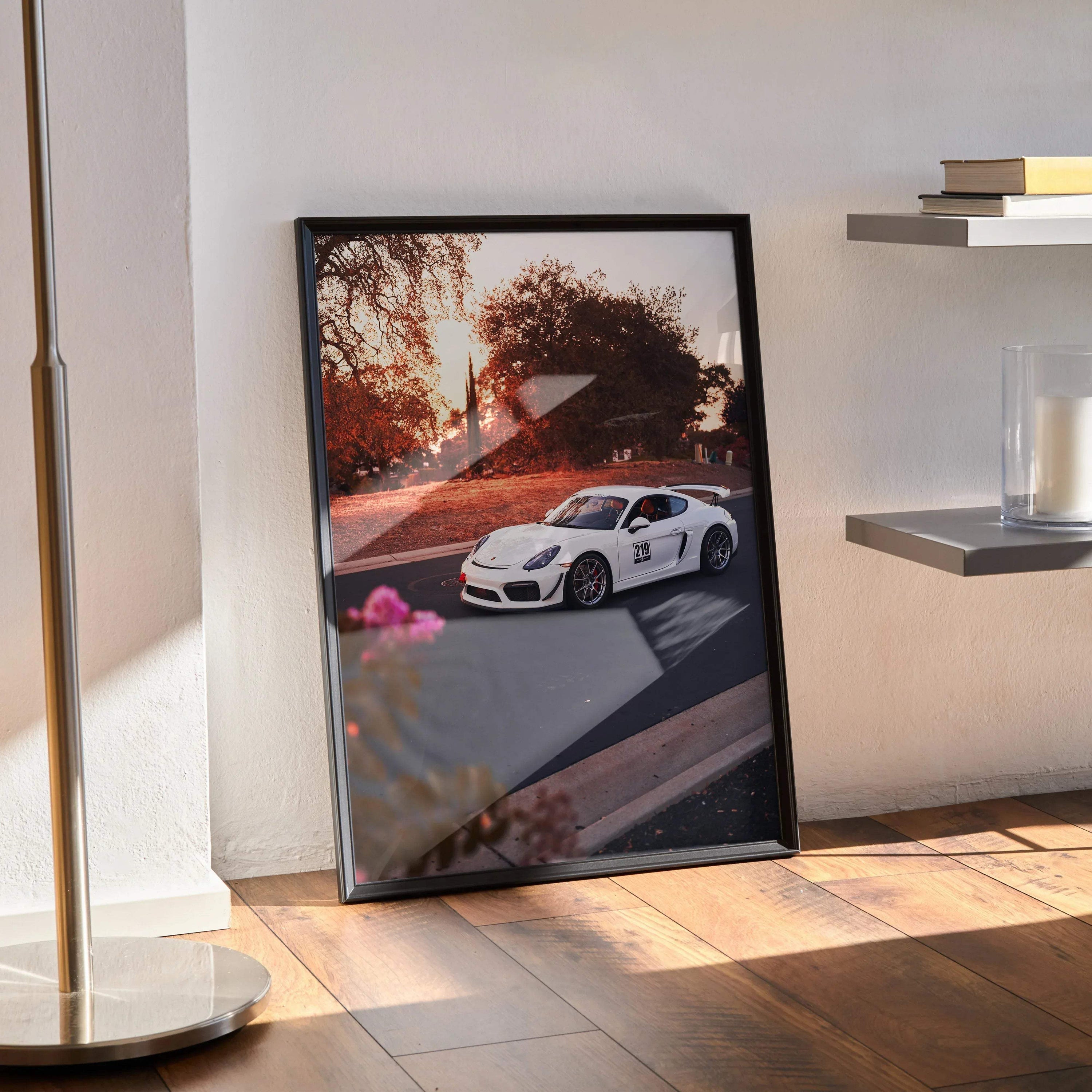 Porsche Cayman GT4 poster with sunset backdrop in sleek black frame leaning on floor wall art.