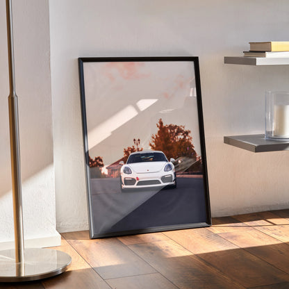 Porsche Cayman GT4 poster with sleek white car and autumn trees, framed wall art leaning on floor.
