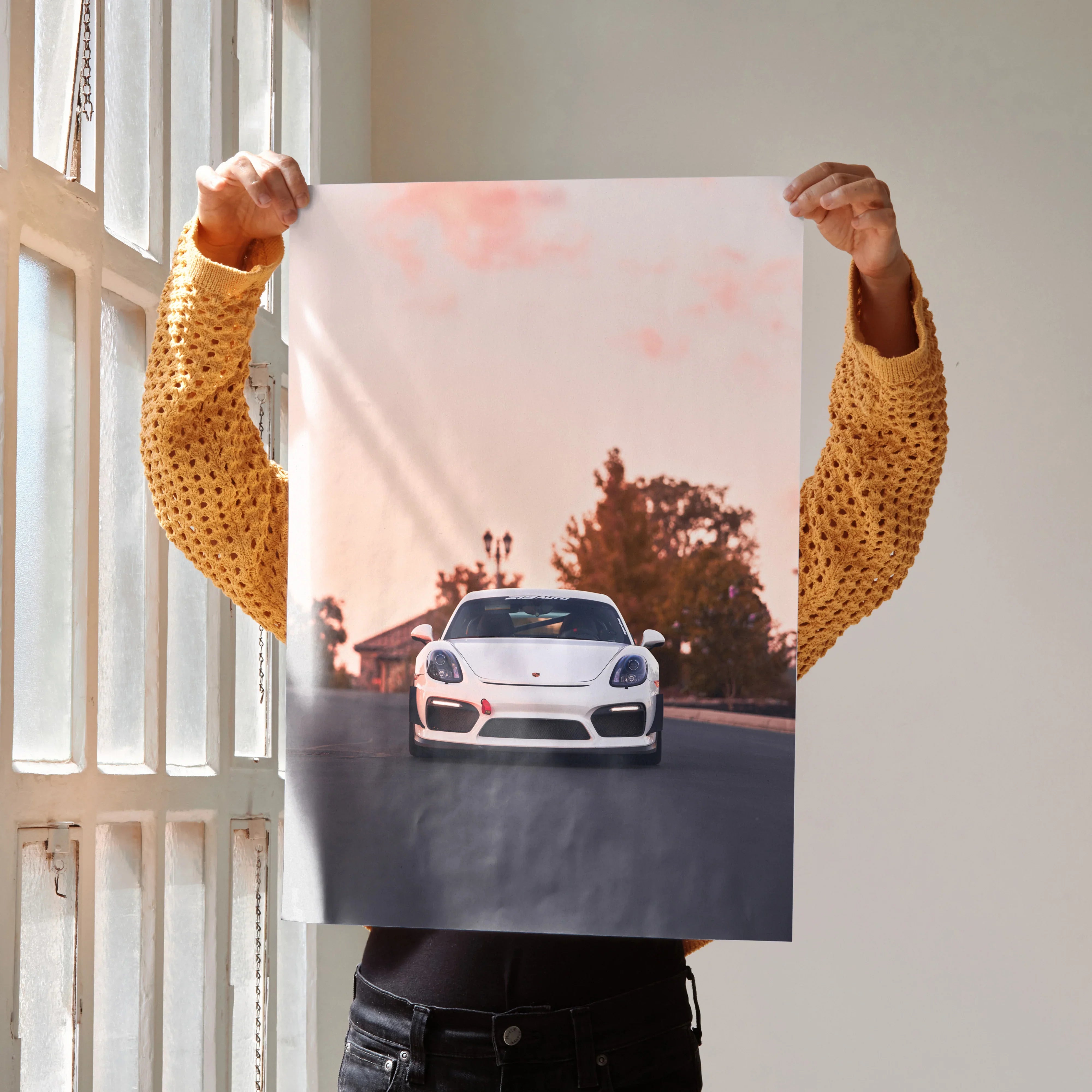 Porsche Cayman GT4 poster held against window with sunset sky and road background wall art.