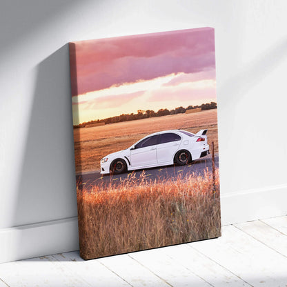 Vertical canvas wall art featuring a white Mitsubishi Evo 10 sports car on a rural road at sunset.