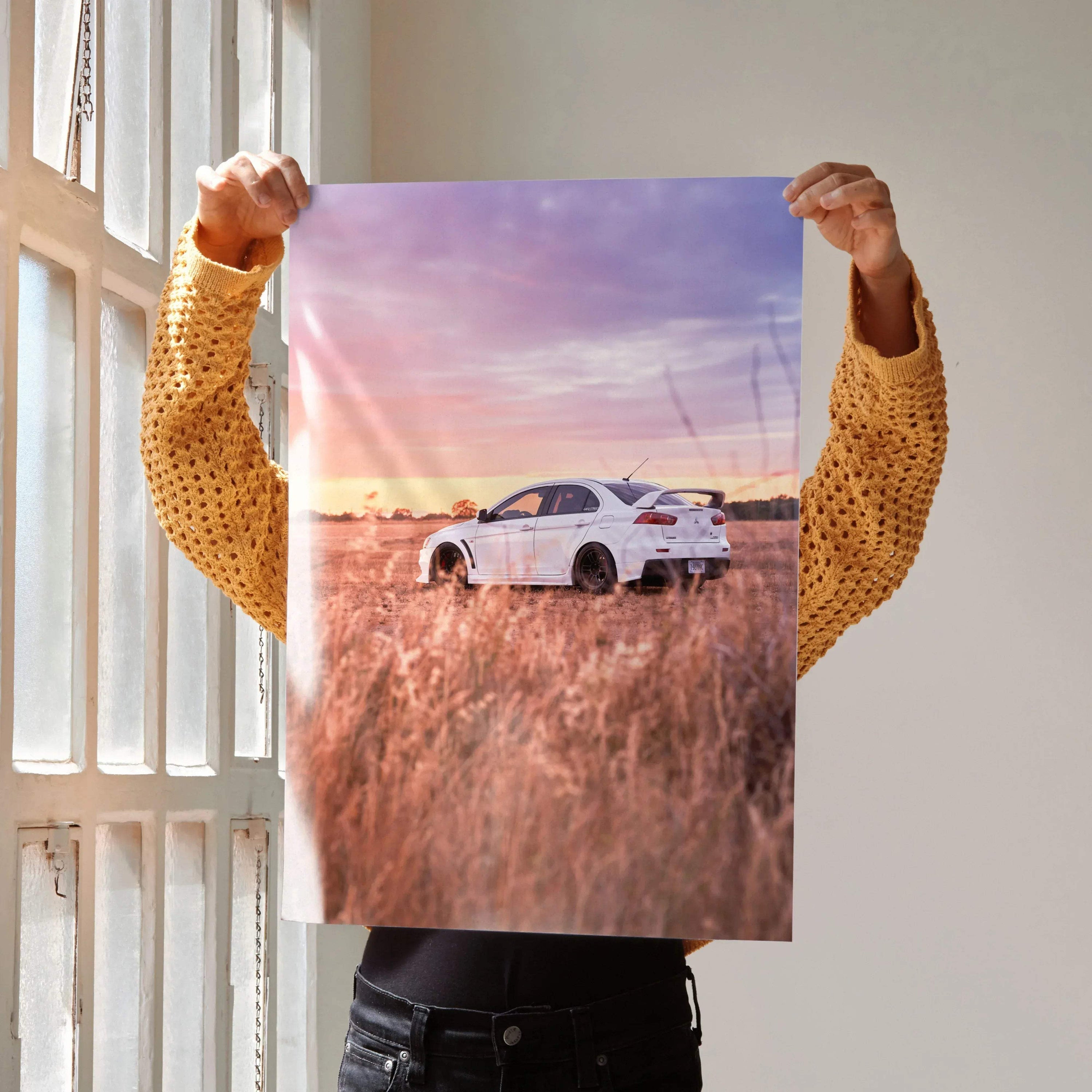 Mitsubishi Evo 10 in tall grass at sunset poster wall art with vibrant purple and orange sky.