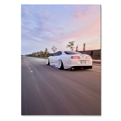 White Toyota Supra MK4 driving on road at sunset, vibrant poster wall art with blurred motion background.