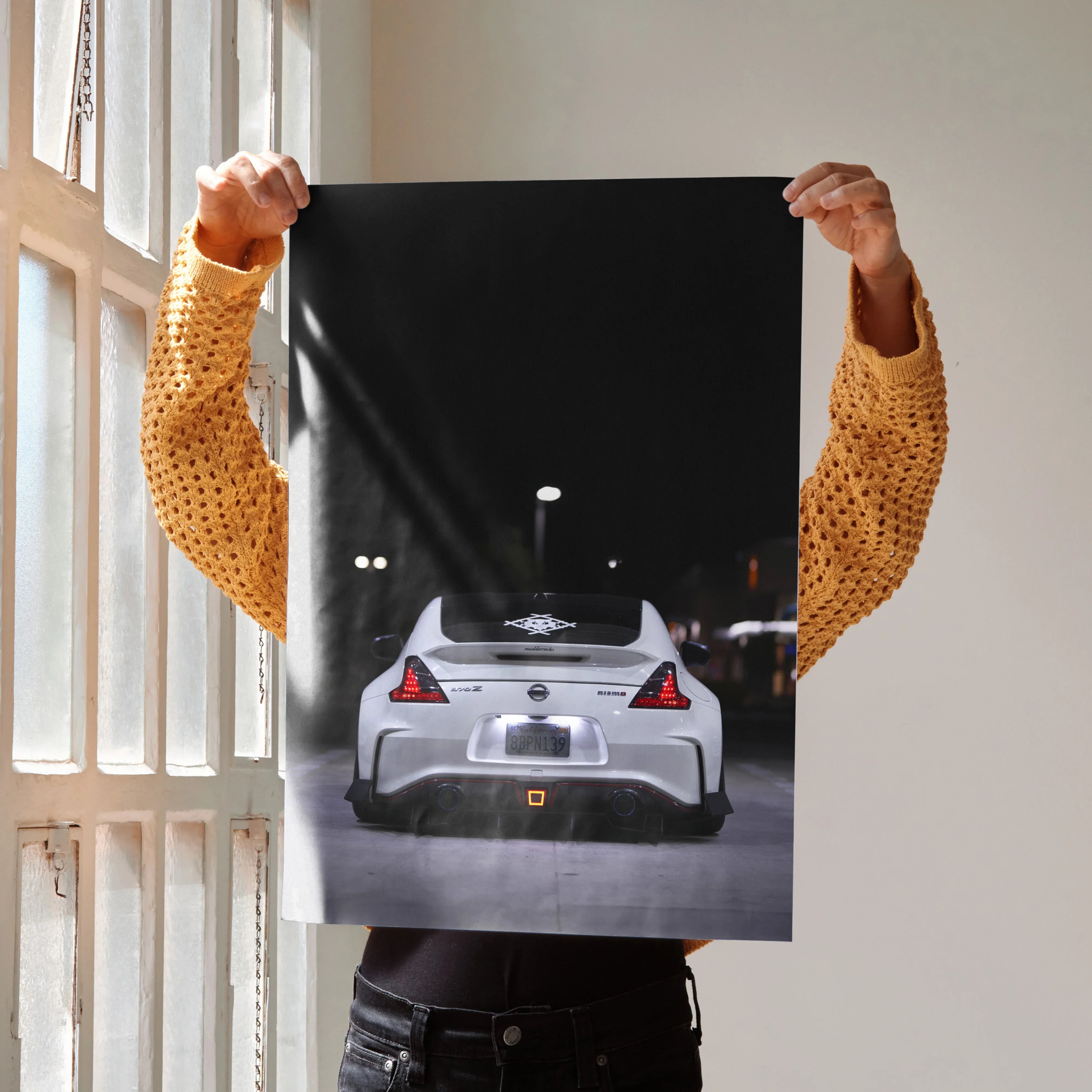Nissan 370z rear view poster held by person in yellow sweater, sleek car wall art on black background.