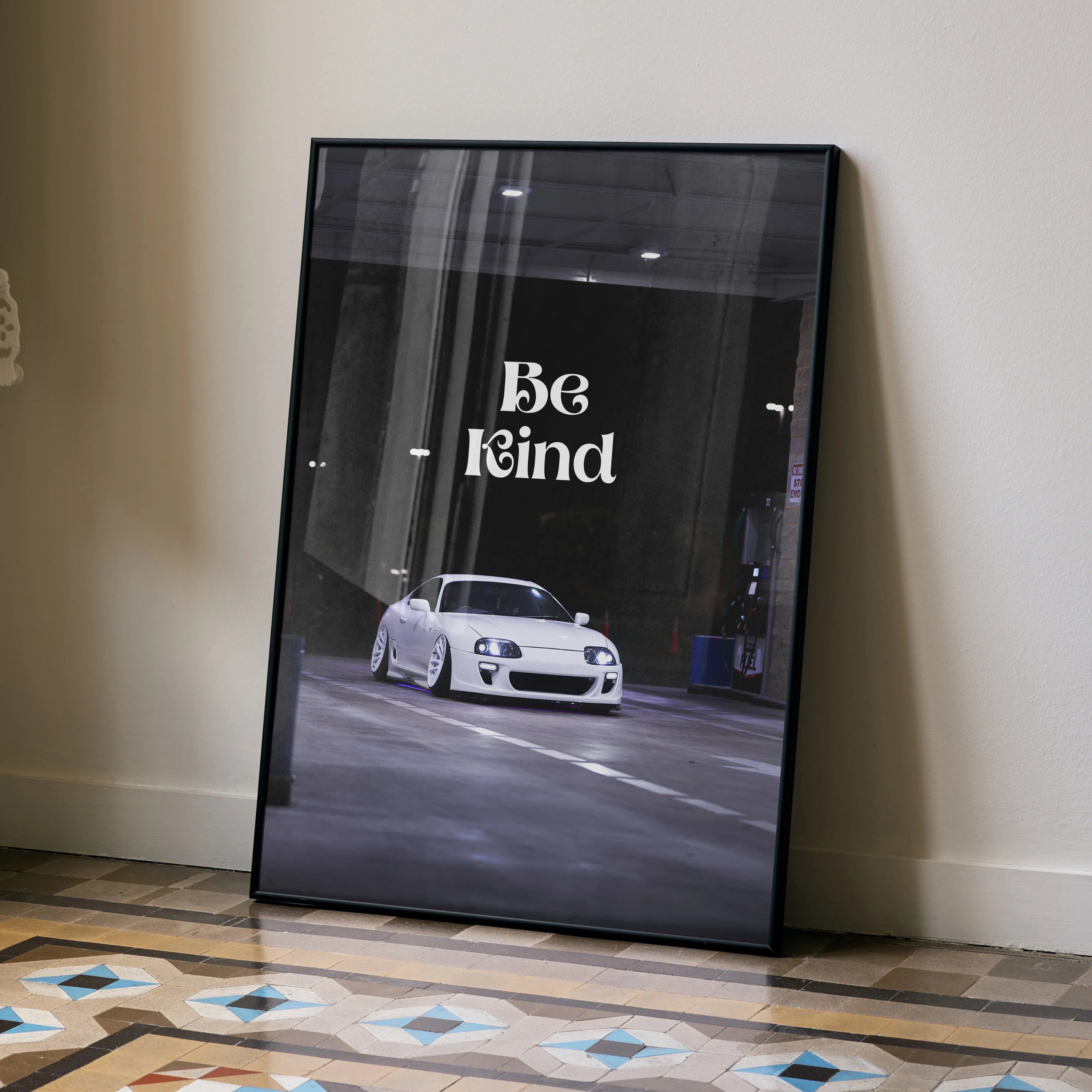Motivational wall art poster featuring a white Toyota Supra Mk4 with "Be Kind" text on dark urban background.