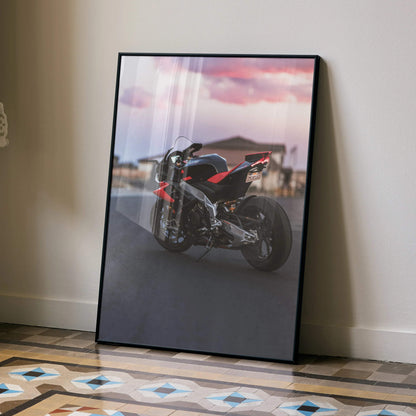 Aprilia RSV4 1100 Factory motorcycle poster with pink sky wall art in black frame leaning on floor.