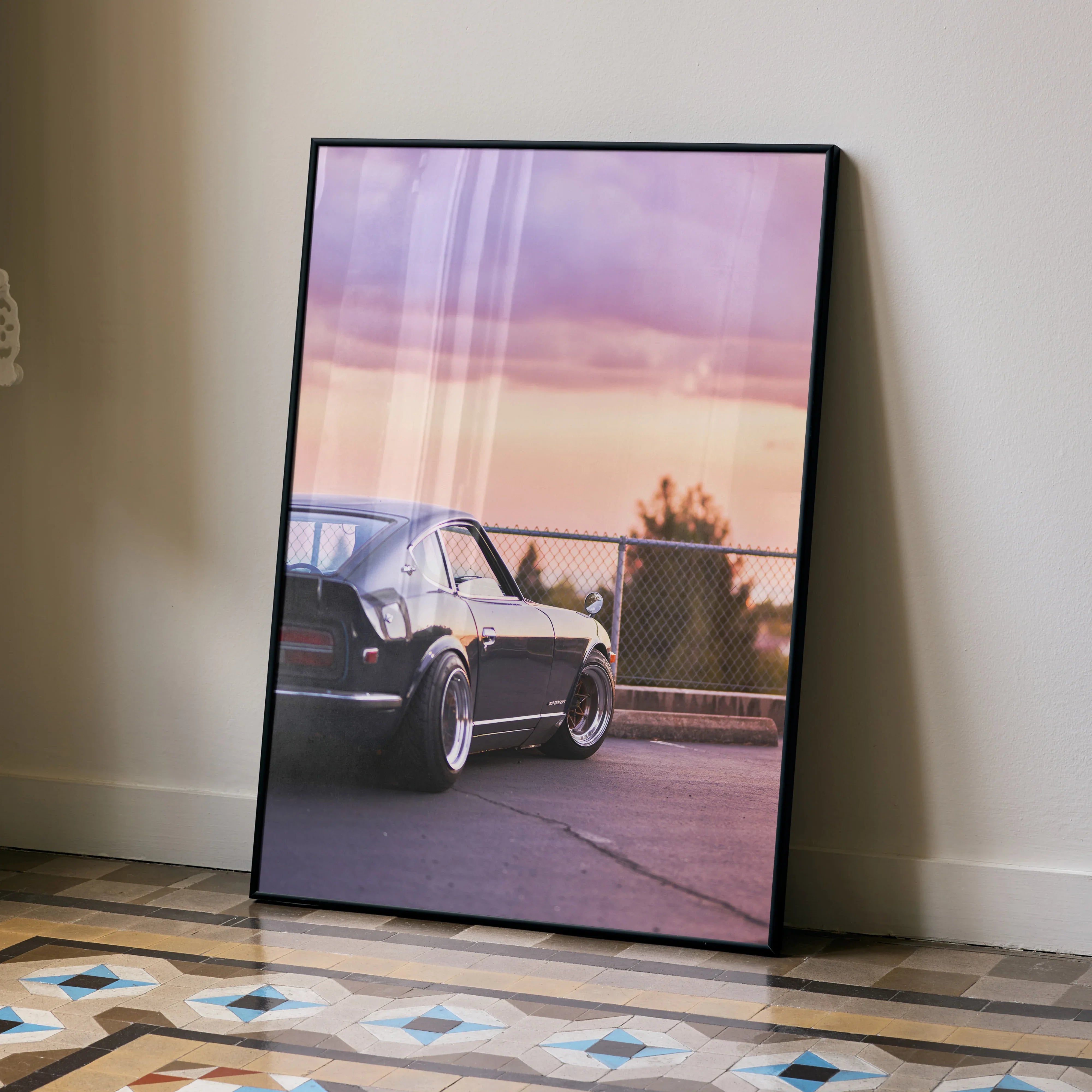 Nissan 240z parked at sunset poster wall art with purple and orange sky backdrop in black frame.
