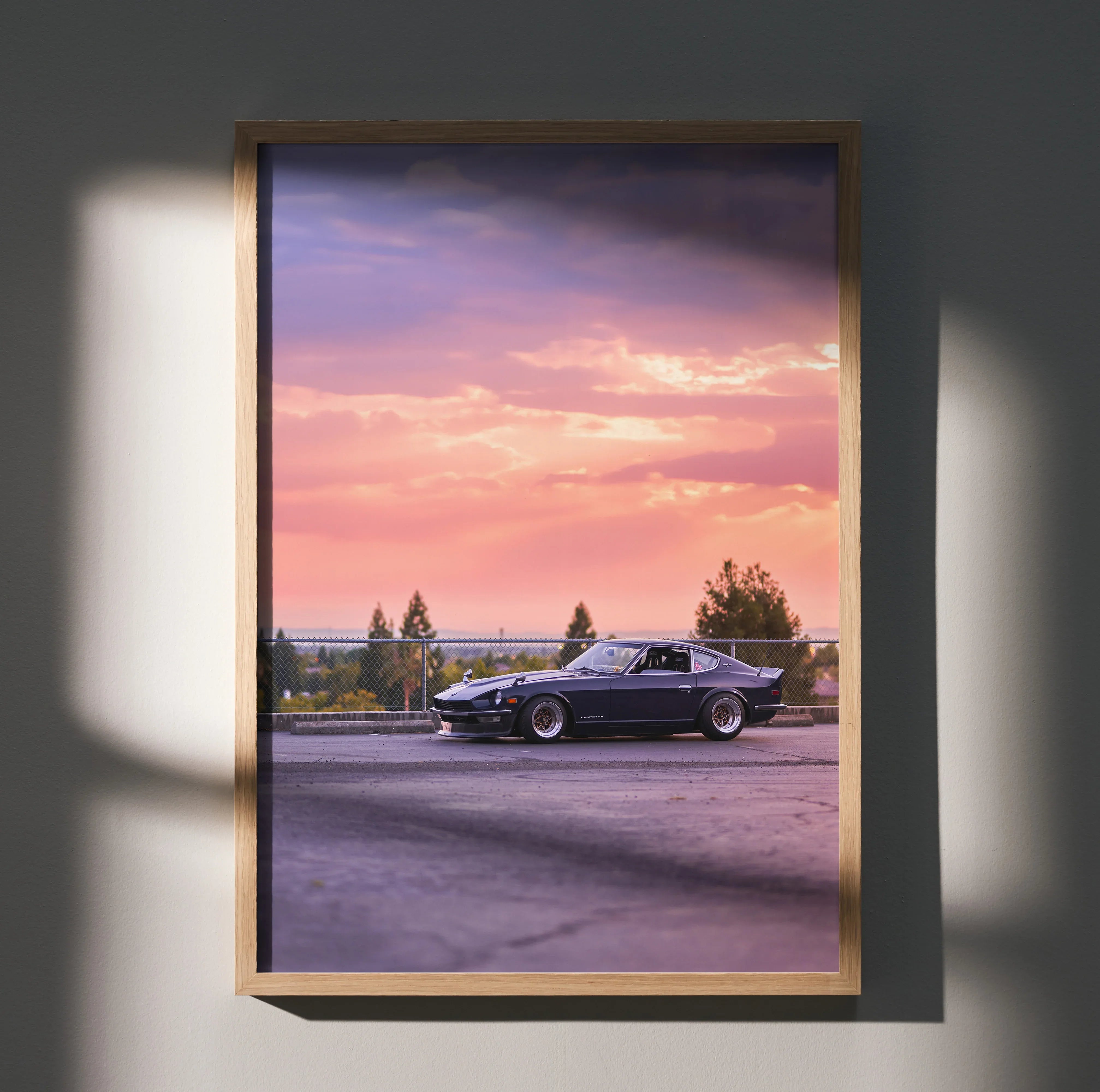Nissan 240z poster wall art with car at sunset framed in wood, vibrant pink and purple sky.