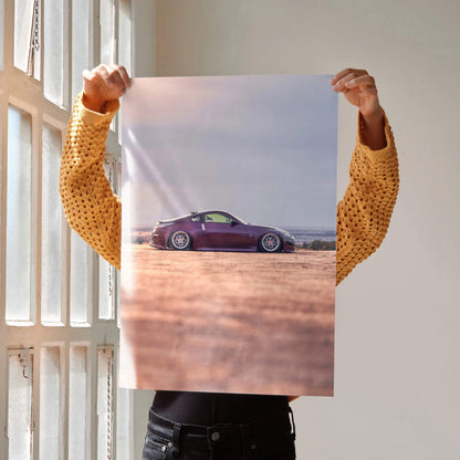 Nissan 350z purple sports car poster held up as wall art with desert landscape background.