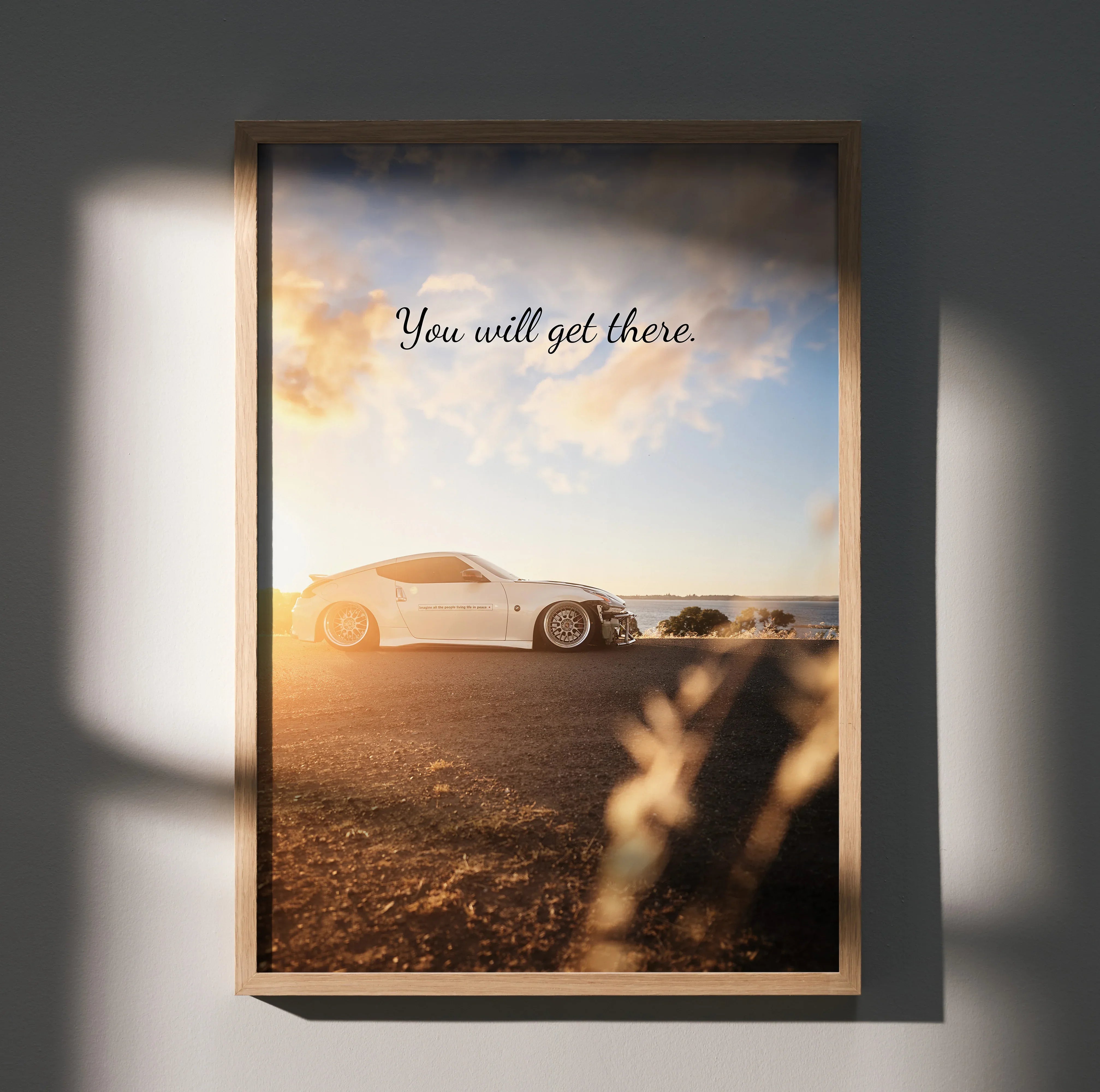 Nissan 370z parked on sunlit road at sunset with motivational text poster wall art.