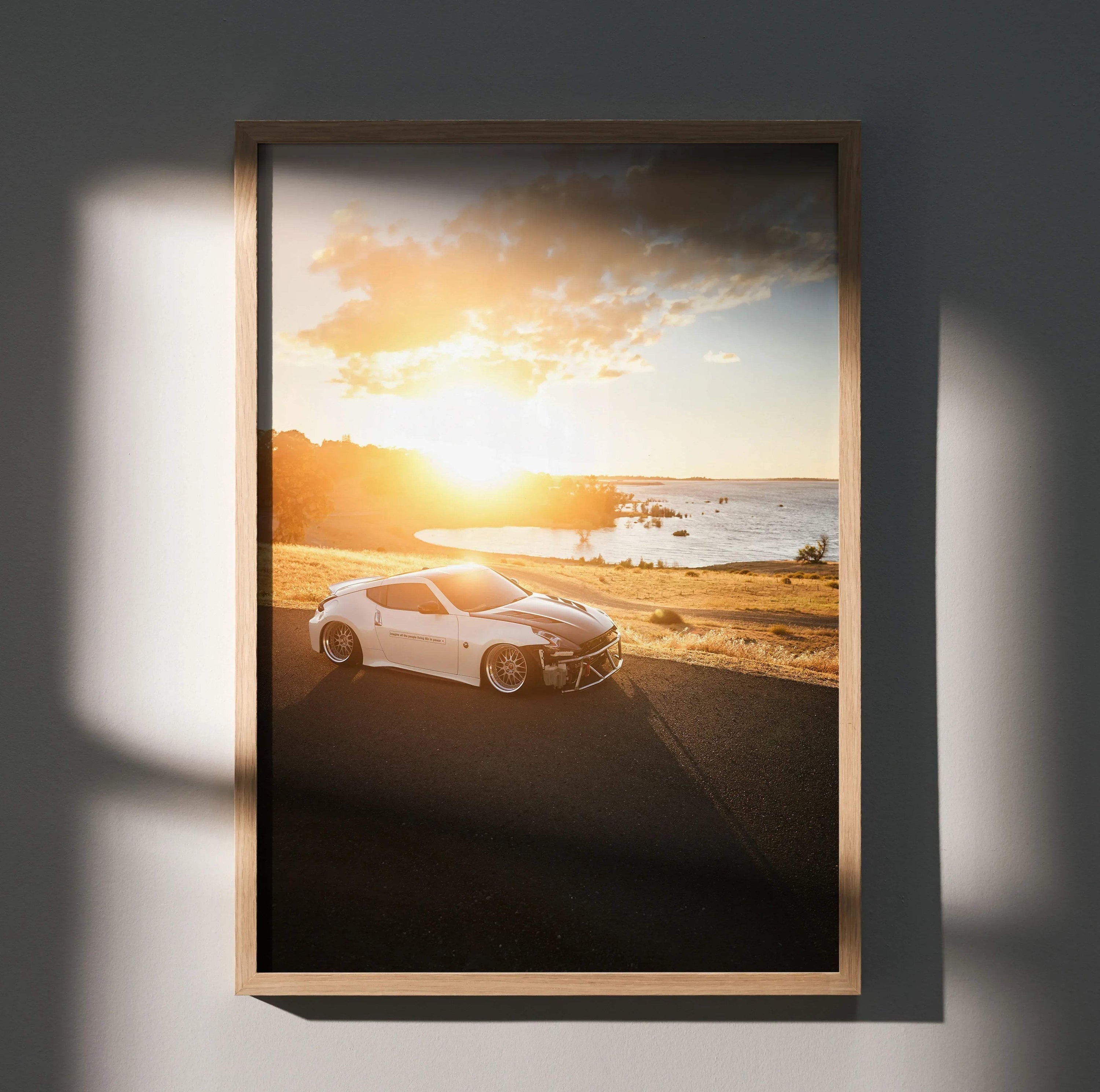 Nissan 370z poster wall art featuring a white sports car parked by a sunlit coastal road at sunset.