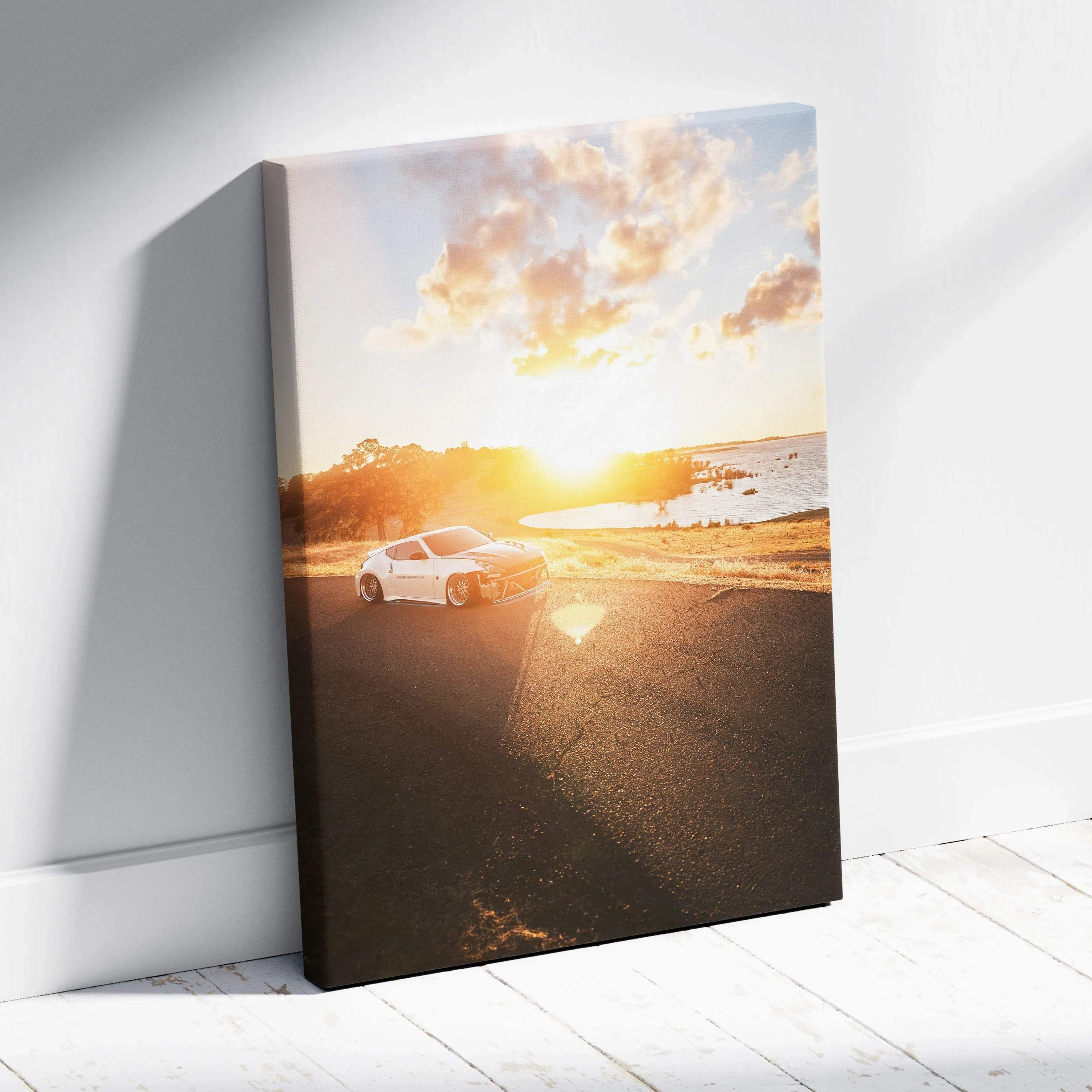 Vertical canvas wall art featuring a white Nissan 370z on a sunlit coastal road at sunset.