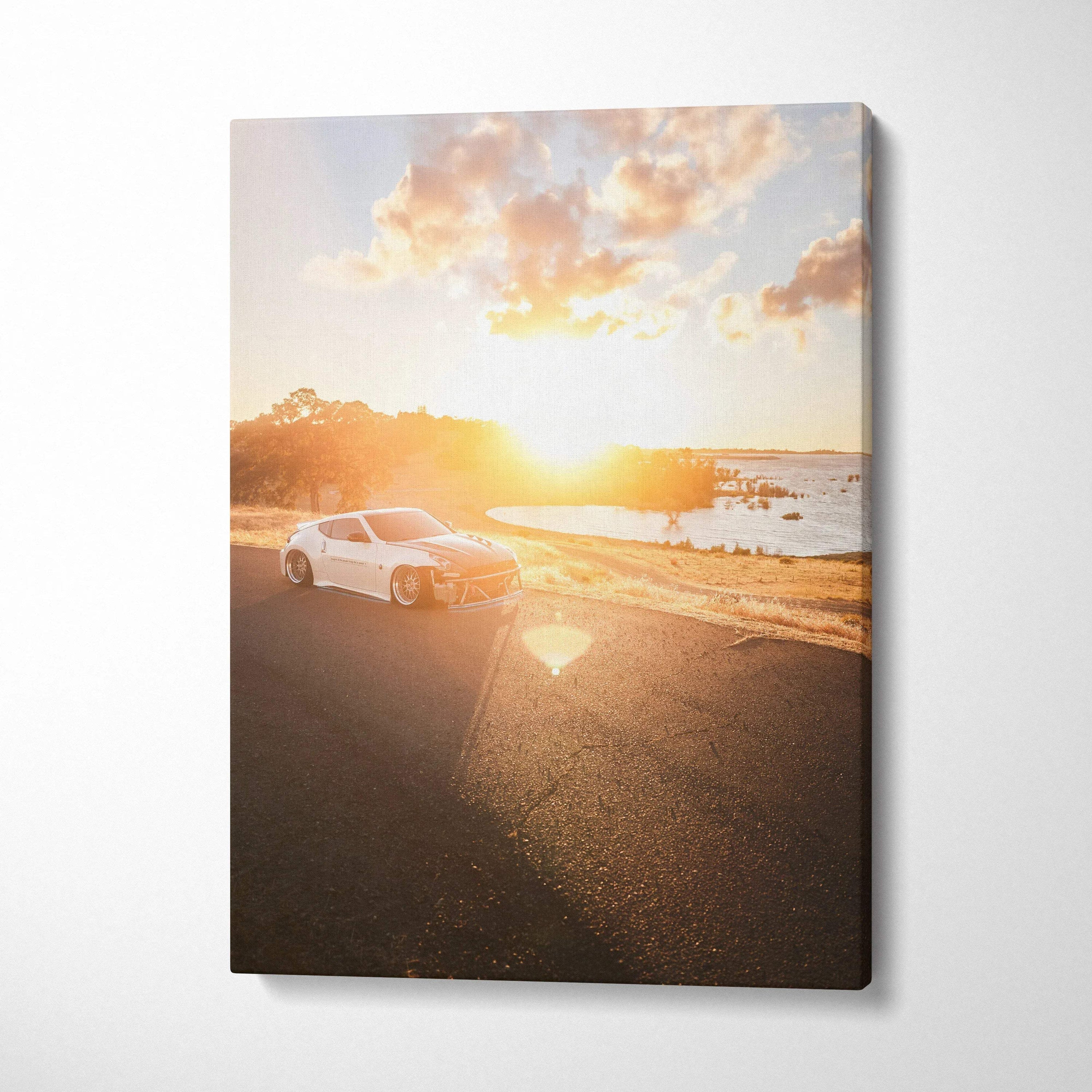 Vertical canvas art featuring a white Nissan 370z on a sunlit coastal road at sunset.