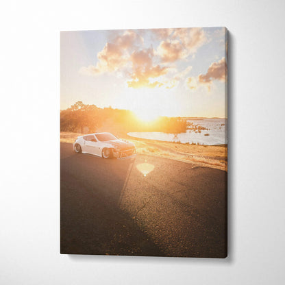 Vertical canvas art featuring a white Nissan 370z on a sunlit coastal road at sunset.