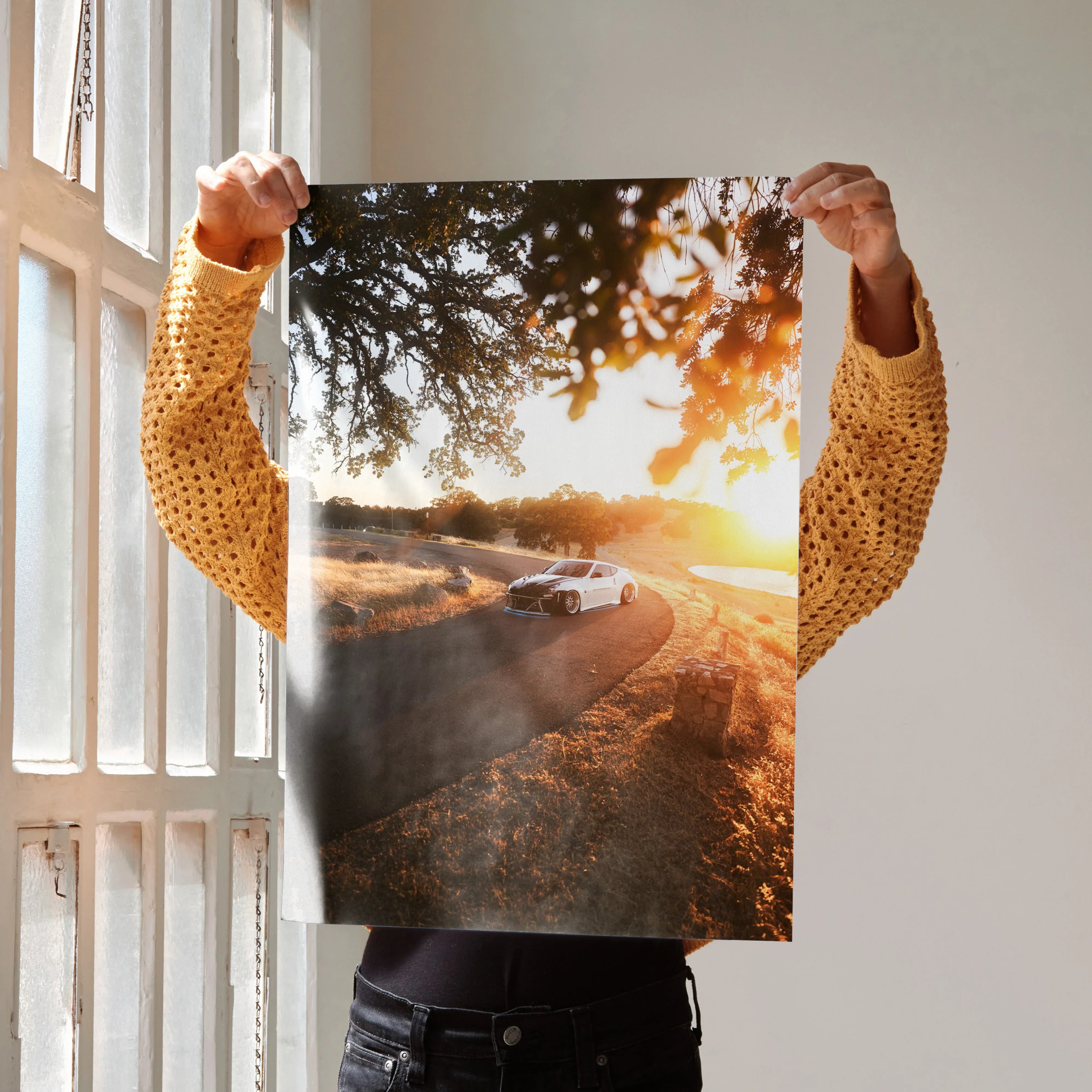 Nissan 370z driving on winding road at sunset poster wall art with golden light and scenic landscape.