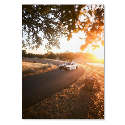 Nissan 370z cruising on winding road at sunset poster wall art with warm golden tones.