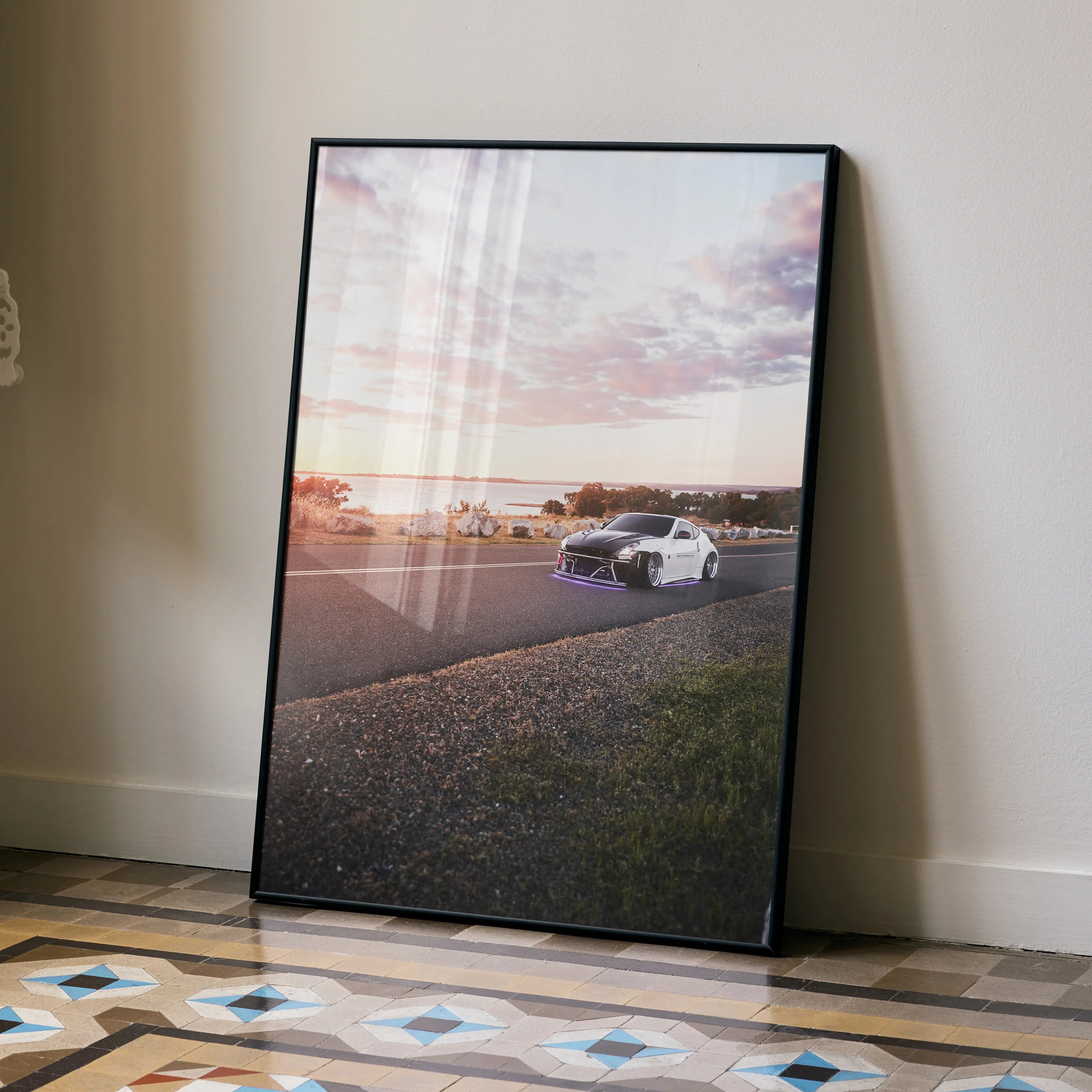 Framed Nissan 370z car poster with sunset sky, displayed as modern wall art on floor.