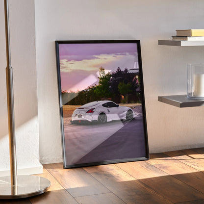 Nissan 370z poster wall art with white sports car at sunset framed in black leaning on floor.